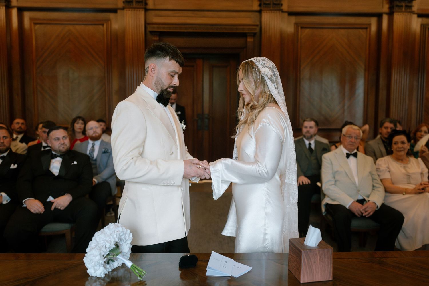 A wedding ceremony taking place in an elegant wood-paneled venue with guests watching.
