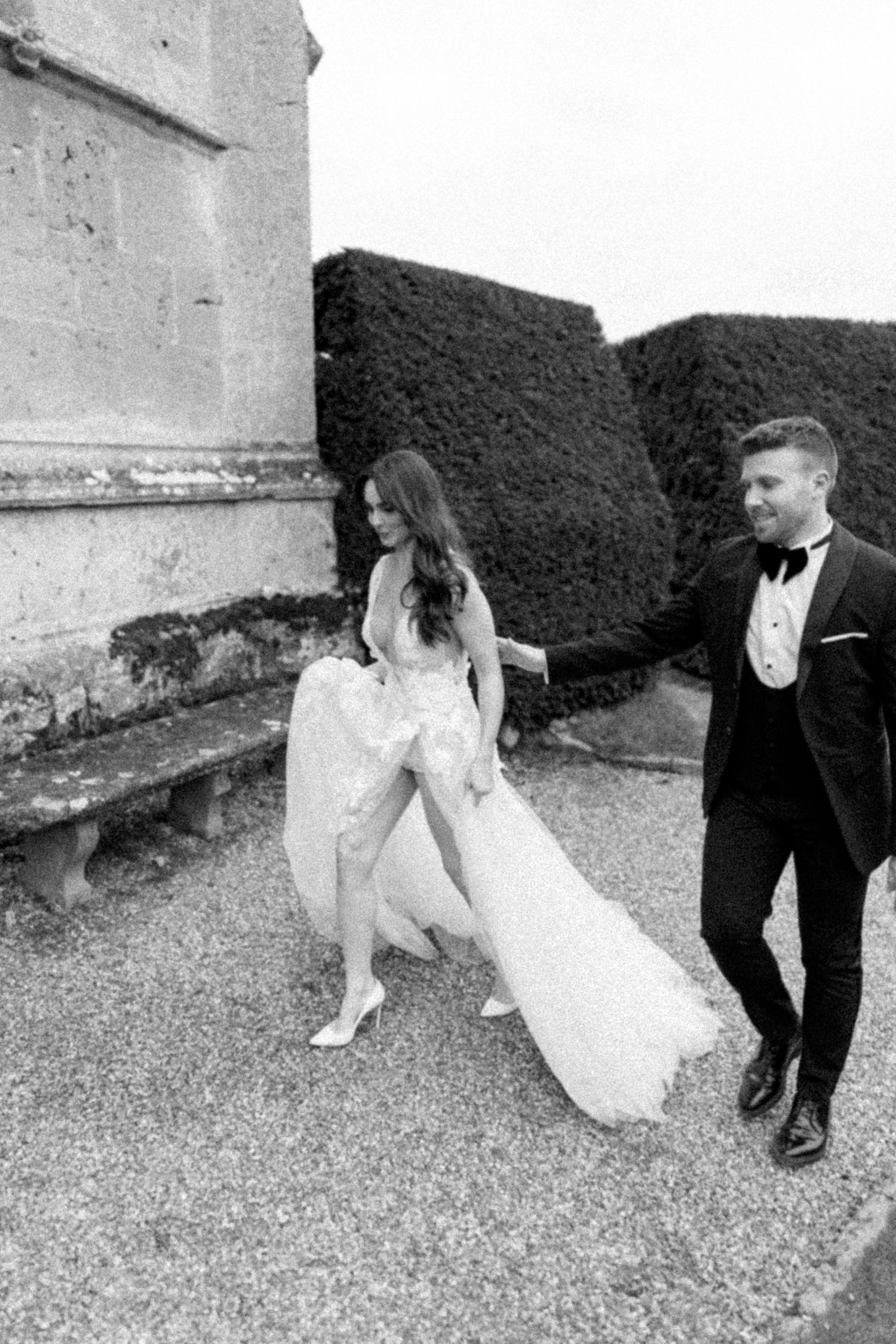 Black and white wedding photos captured on gravel path beside stone wall.