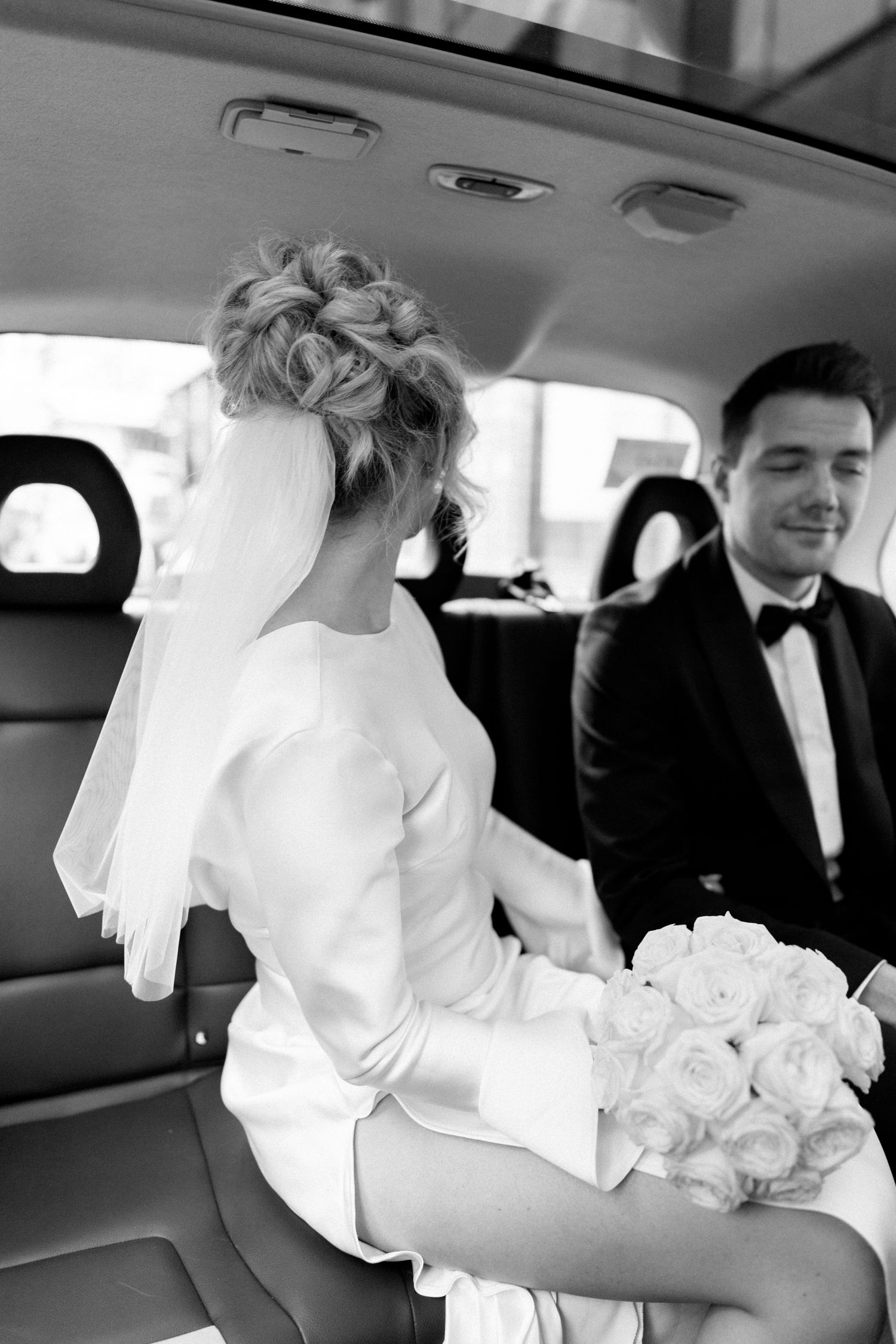 A wedding couple shares a moment in the back of a luxury car with white roses.