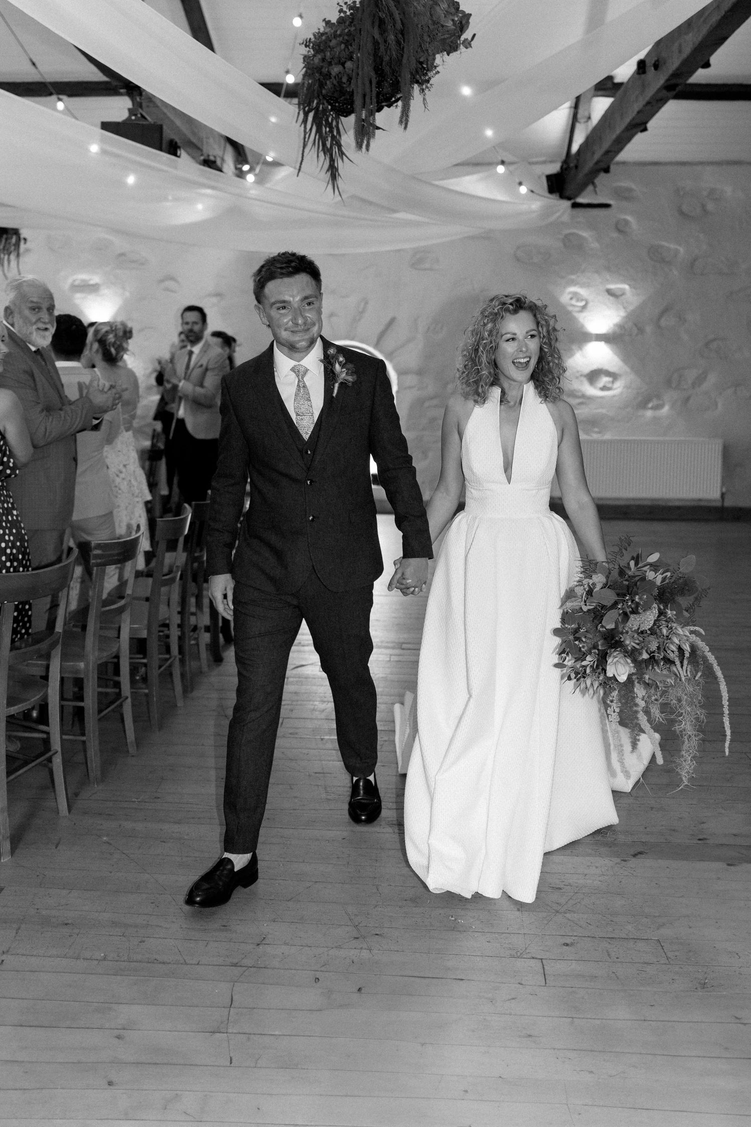 Black and white photo showing wedding guests dancing and celebrating in a decorated reception hall.