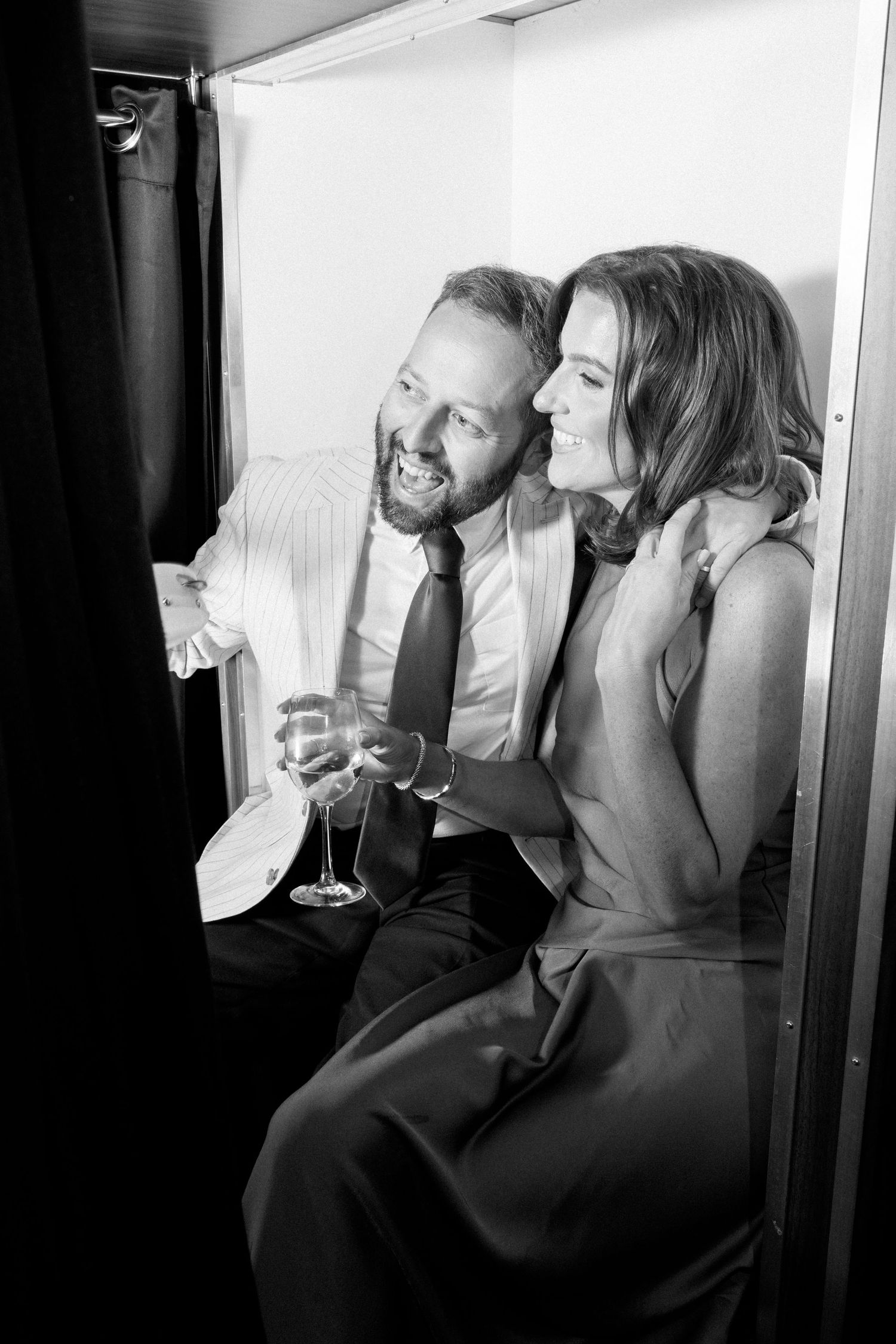A candid black and white photo of a couple sharing drinks and laughter.