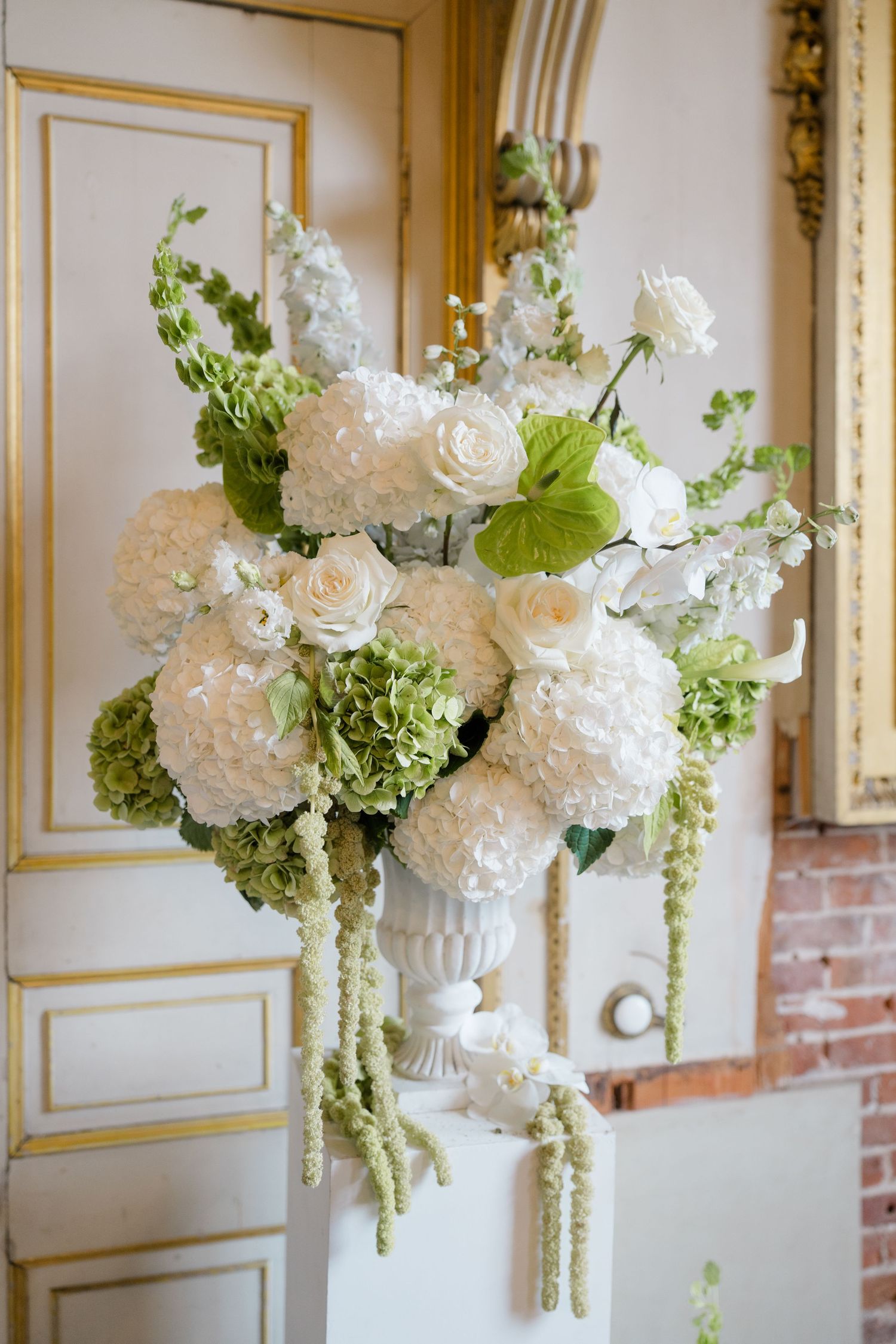Elegant white floral arrangement with hydrangeas and roses in a white urn vase at a wedding venue.