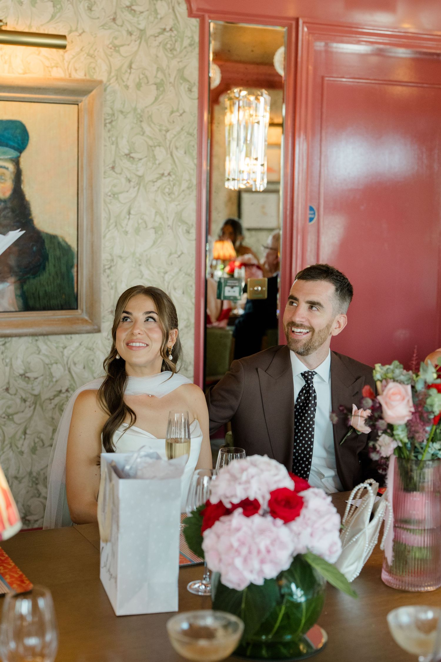 Bride and groom smiling at wedding reception table with champagne and pink floral centerpieces.