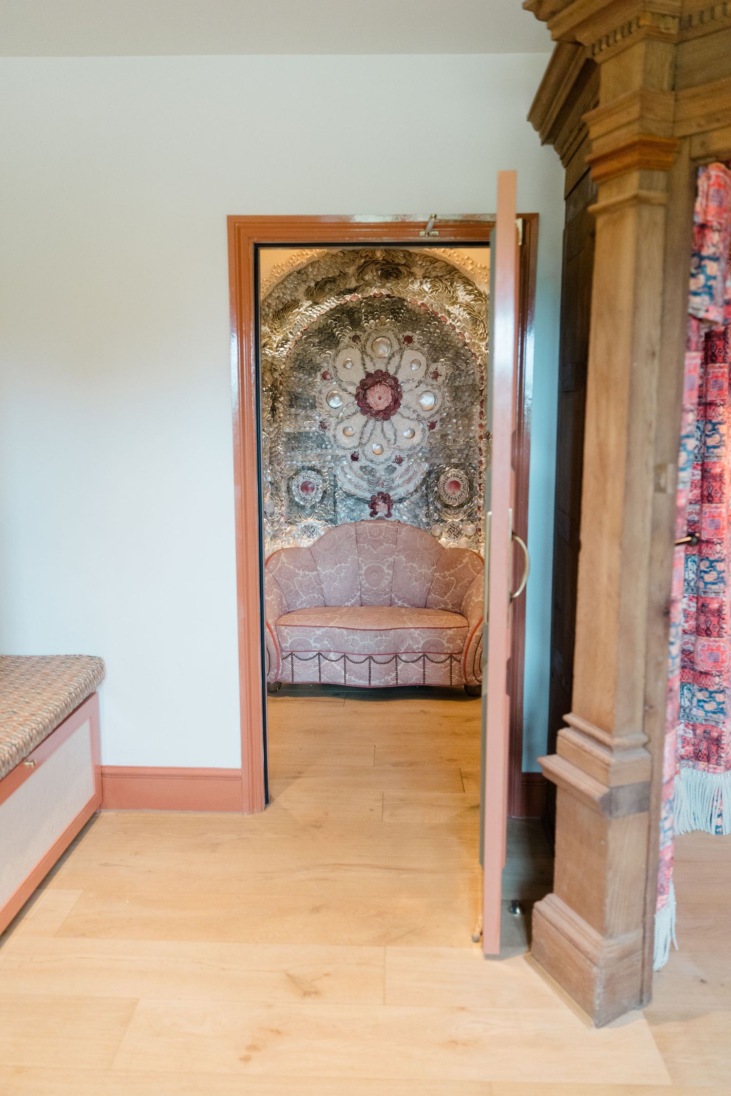 Ornate doorway revealing a decorative alcove with mosaic ceiling, pink sofa, and intricate floral tile work beyond.