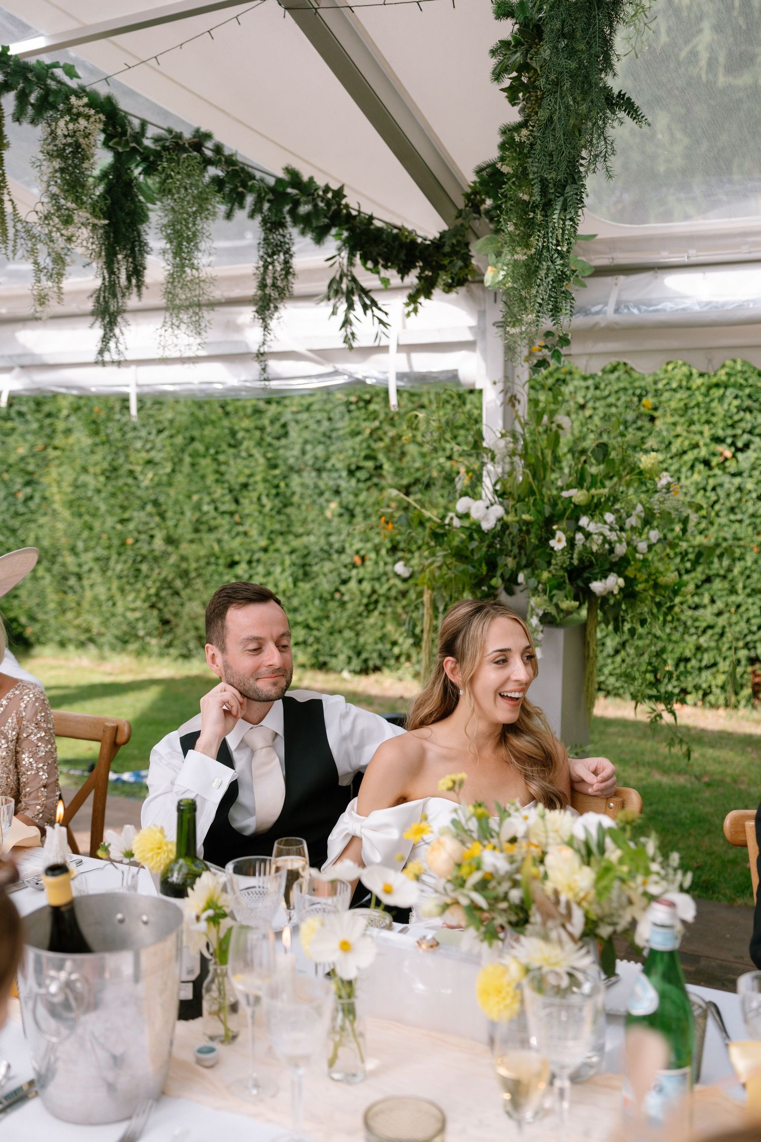 Wedding reception under a greenhouse tent with ivy-covered walls and elegant table settings.