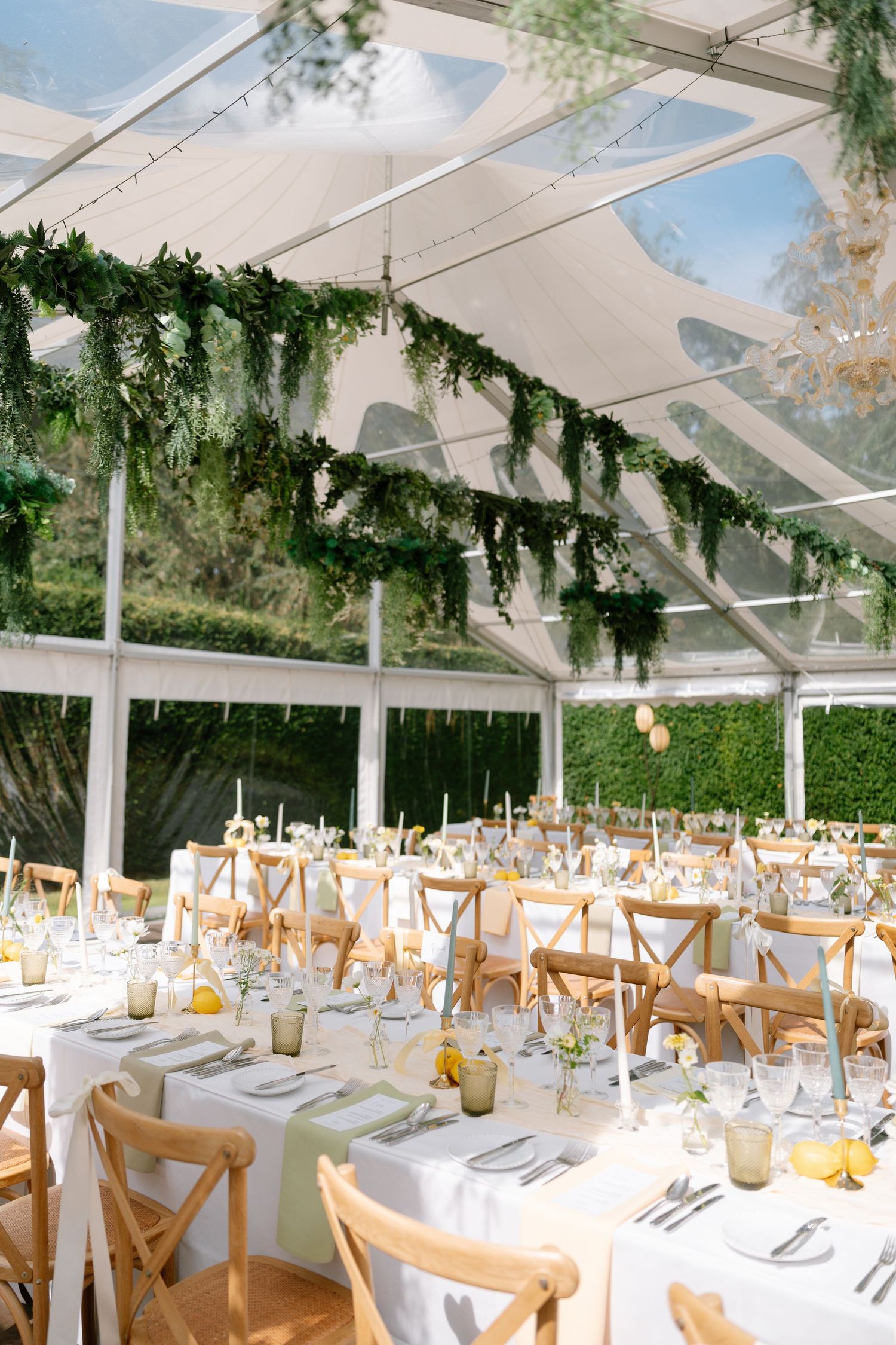 Large clear tent wedding venue with wooden cross-back chairs and white table settings.