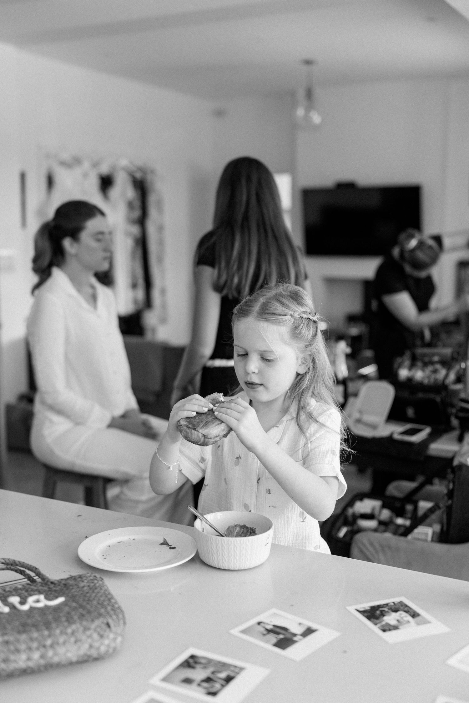 Child eating at white table with photographs spread out.
