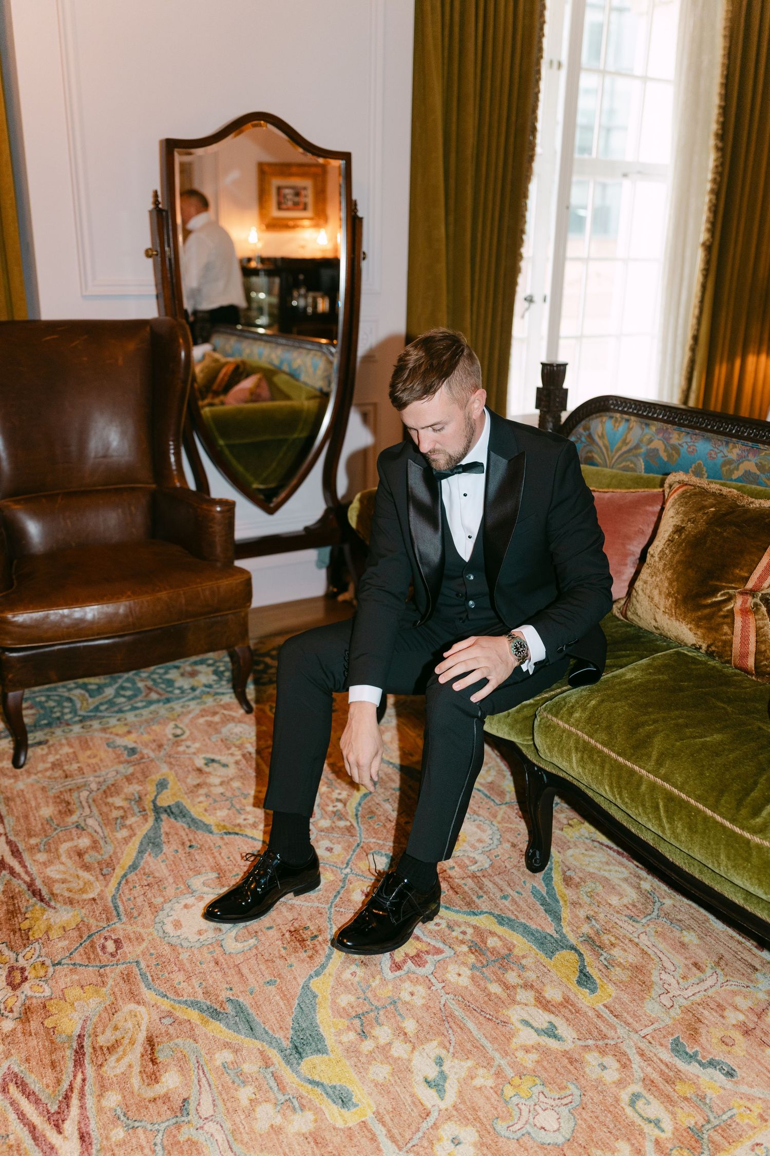 Person in formal wear sitting on an antique couch with ornate floral carpet beneath.