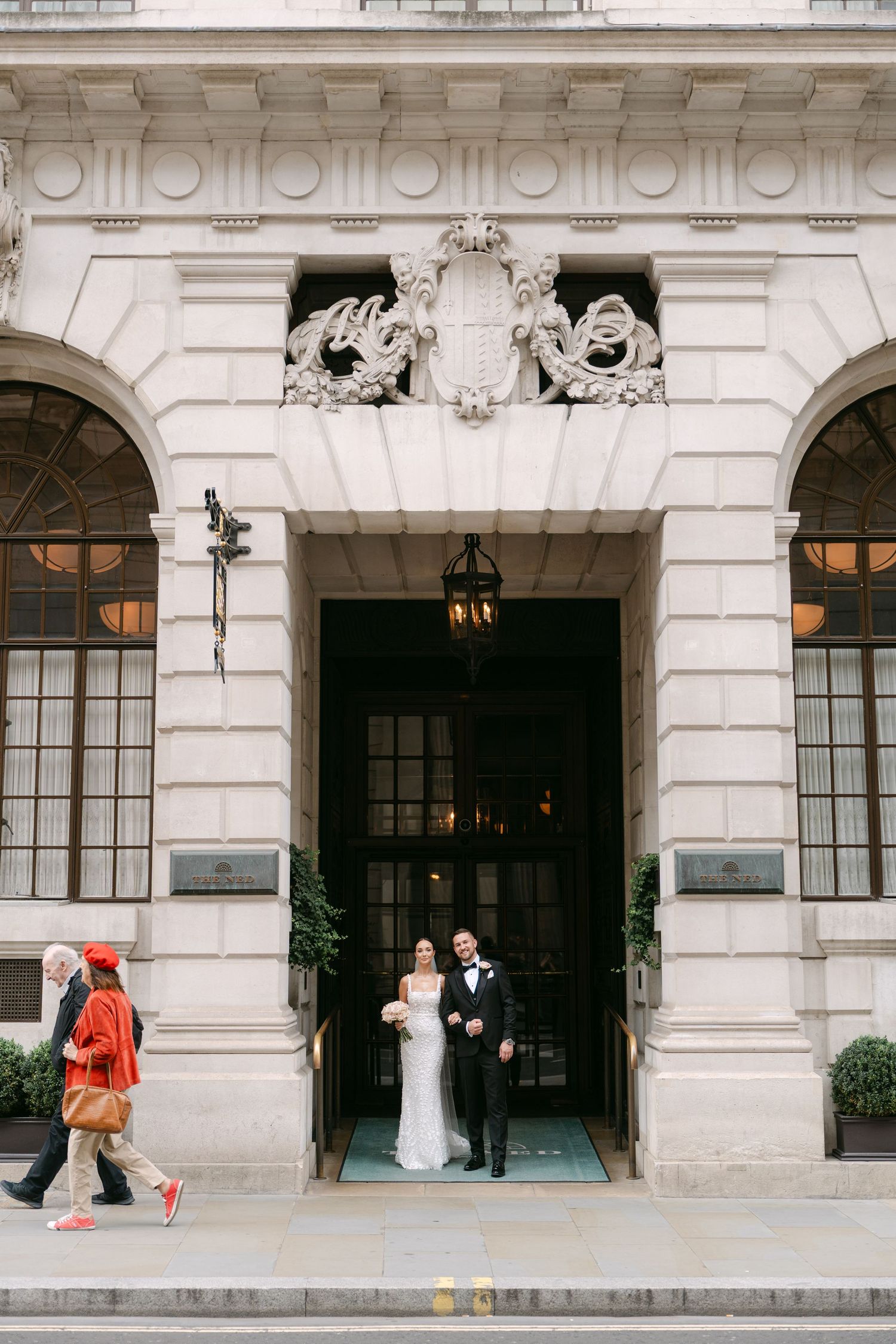 Wedding photograph at an ornate building entrance with decorative stone carvings and large windows.