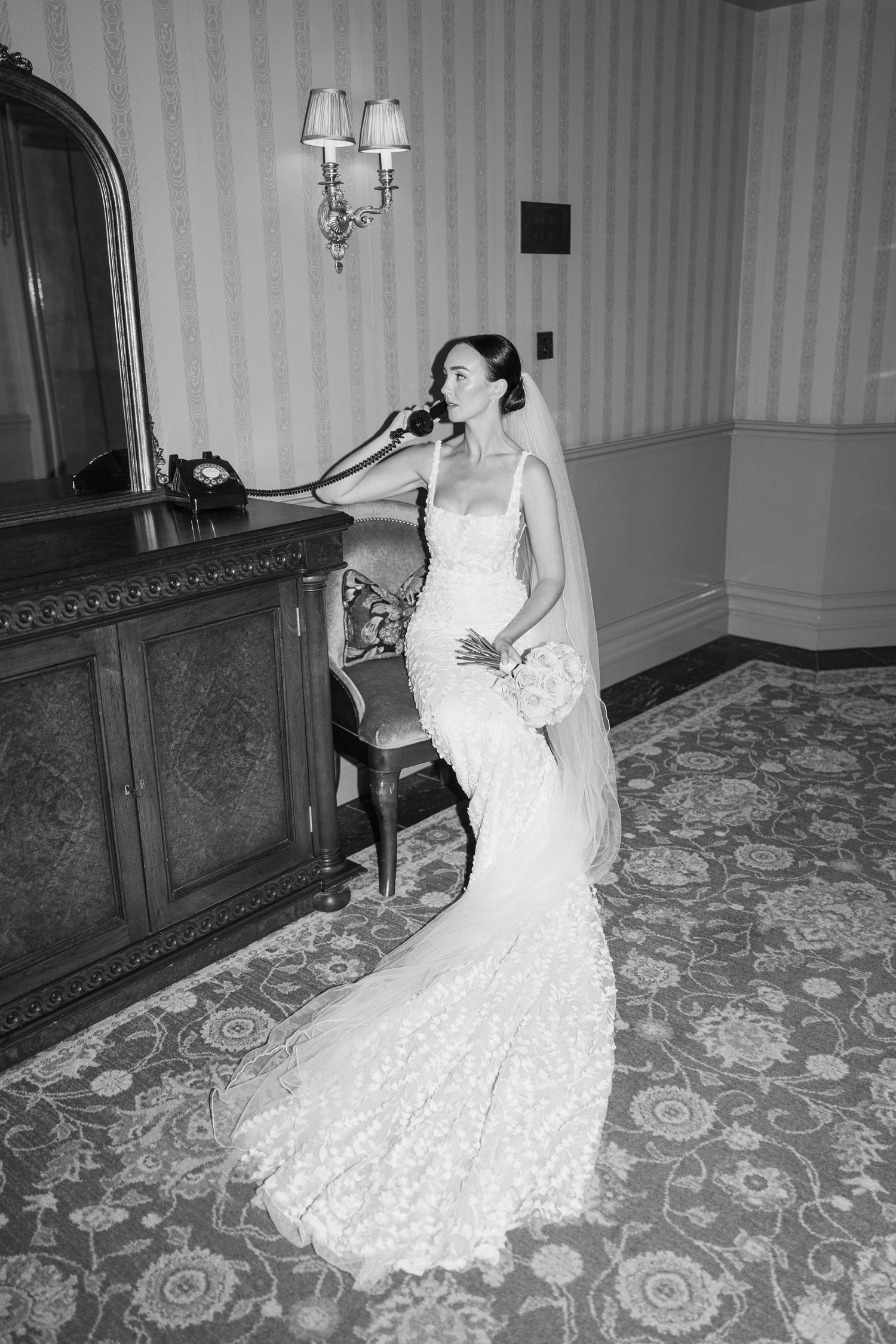 Bride in lace gown poses dramatically against vintage wooden furniture.