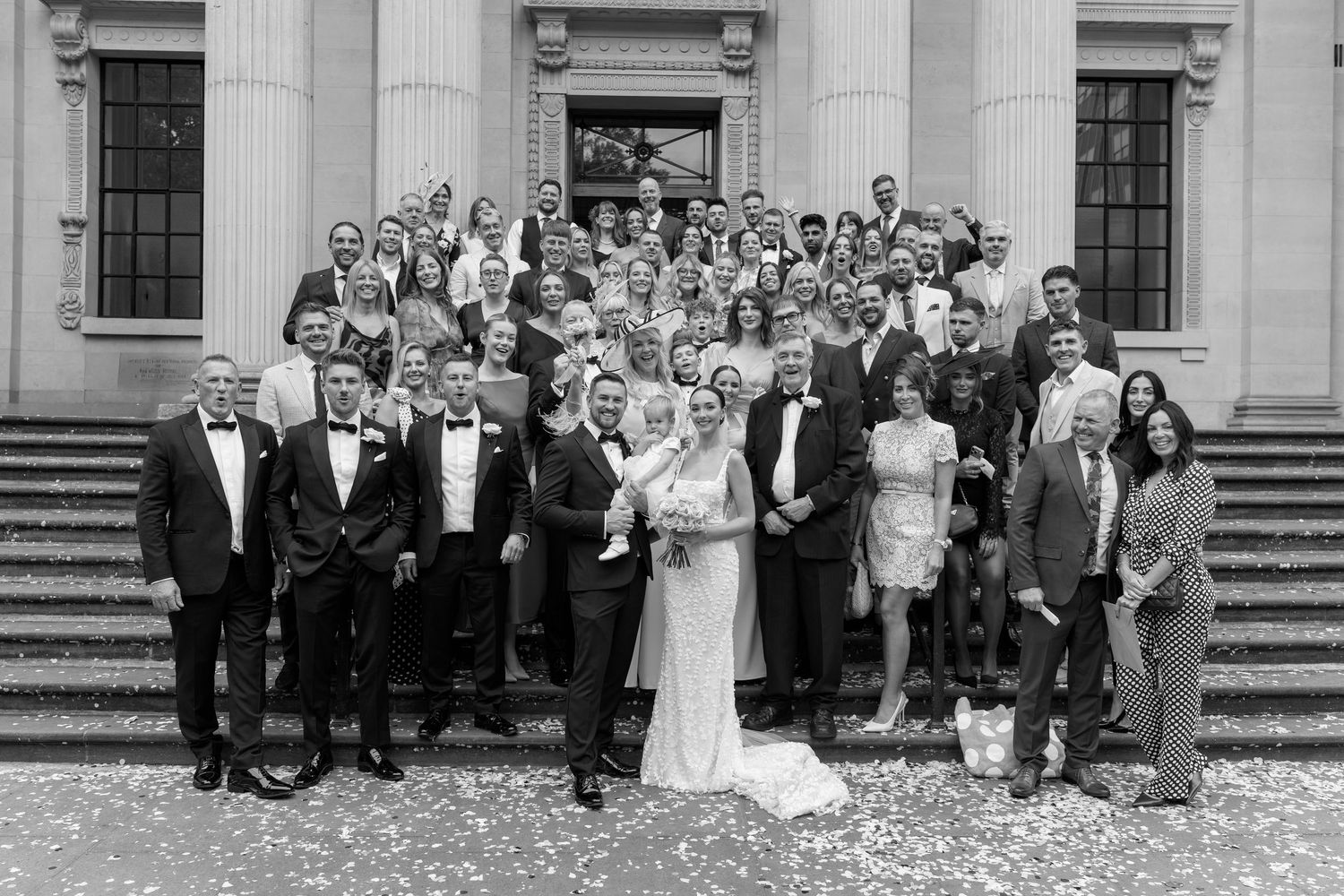 Large group wedding photo on the steps of a classical building with white columns.