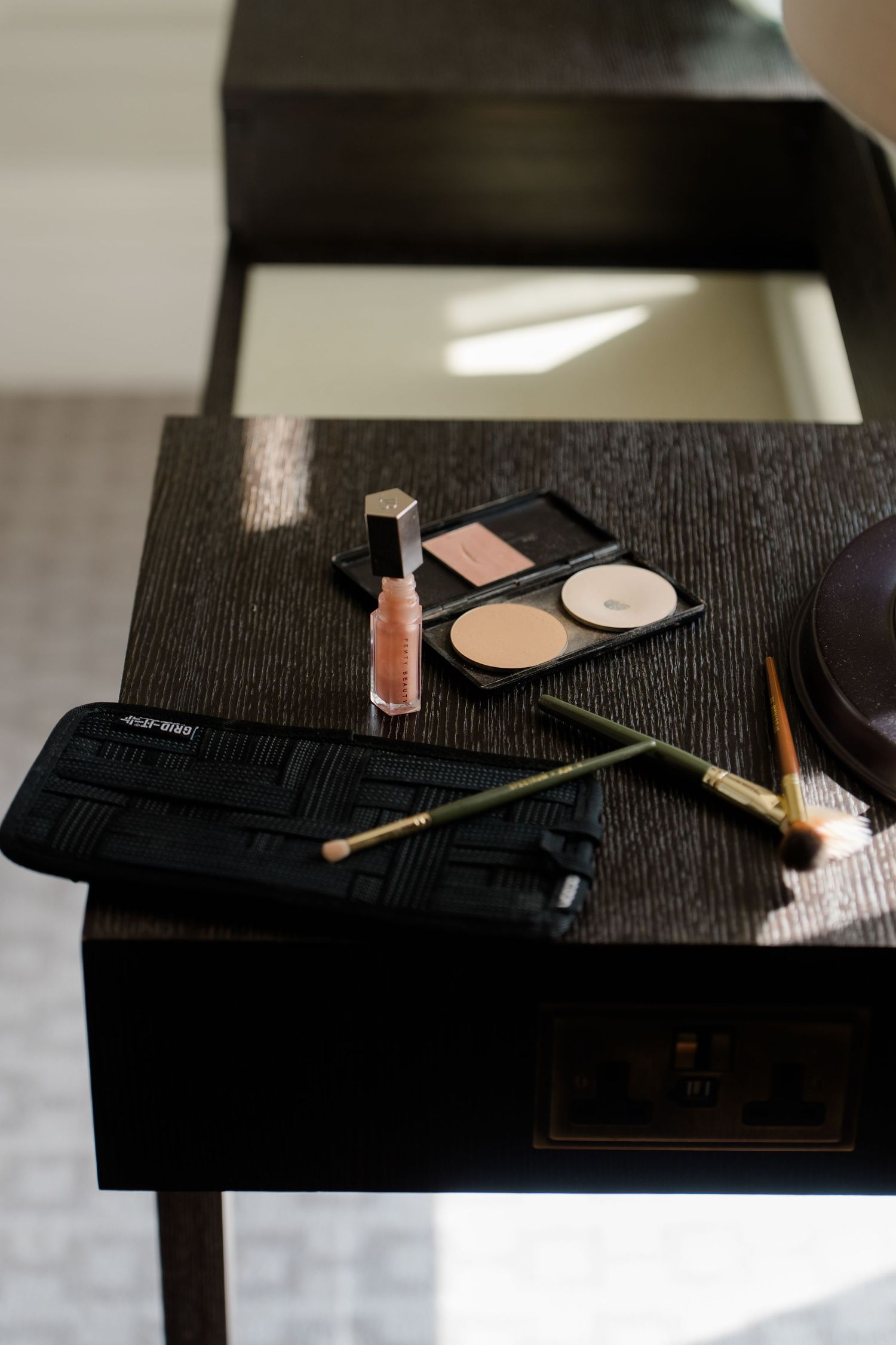 Wedding day makeup essentials including brushes, blush palette, and lip gloss on a dark vanity table.