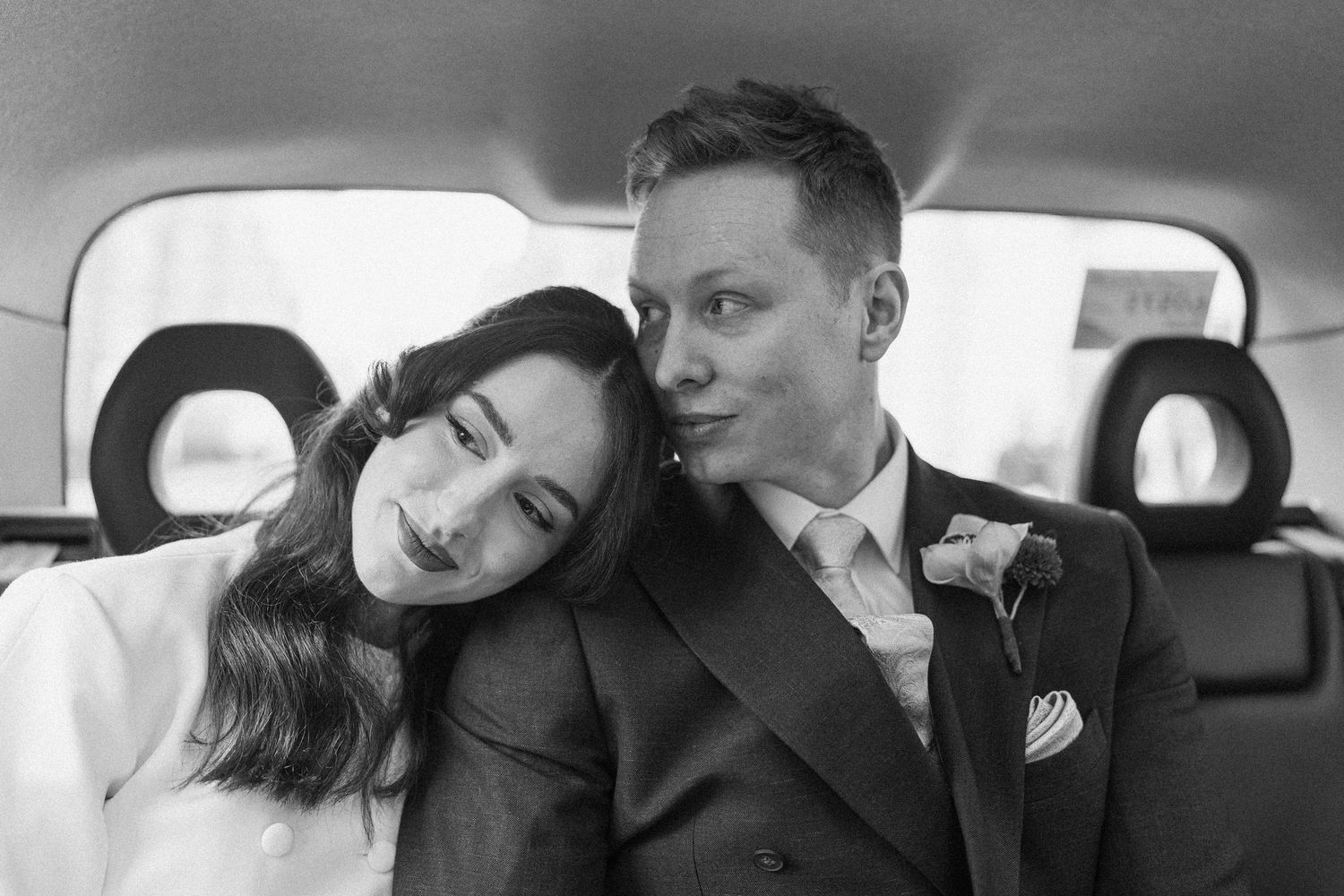 Intimate black and white portrait of newlywed couple sitting together in the back of a wedding car.