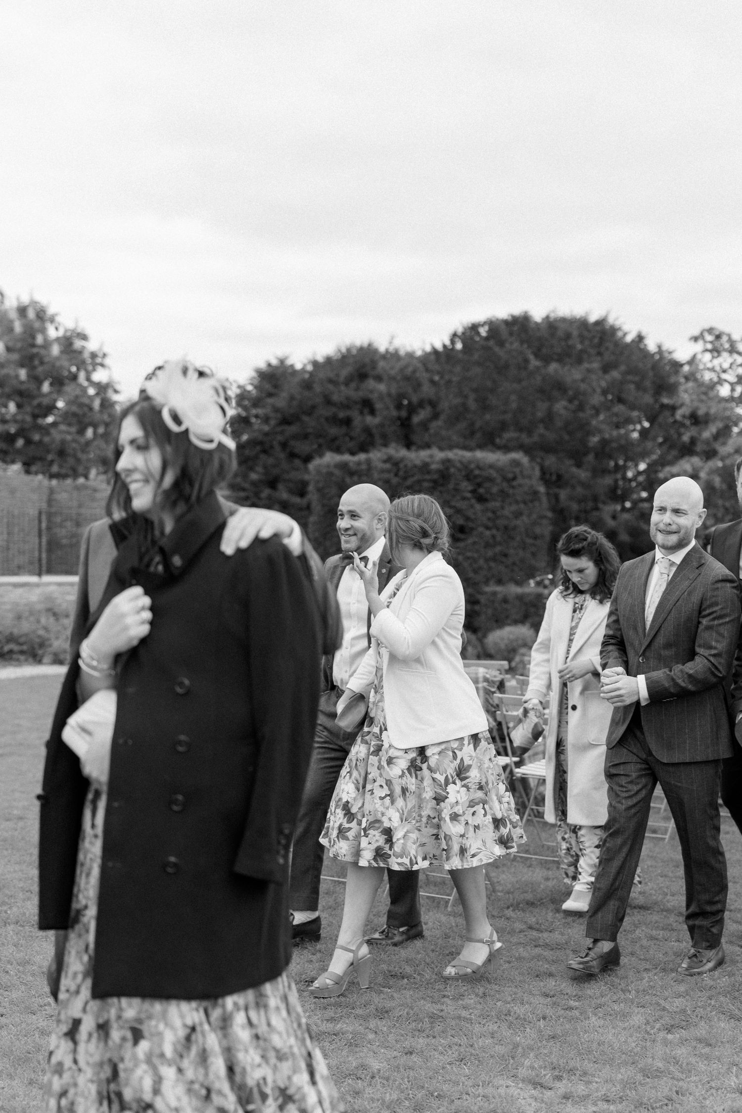 Black and white photo of elegantly dressed wedding guests socializing on a garden lawn.