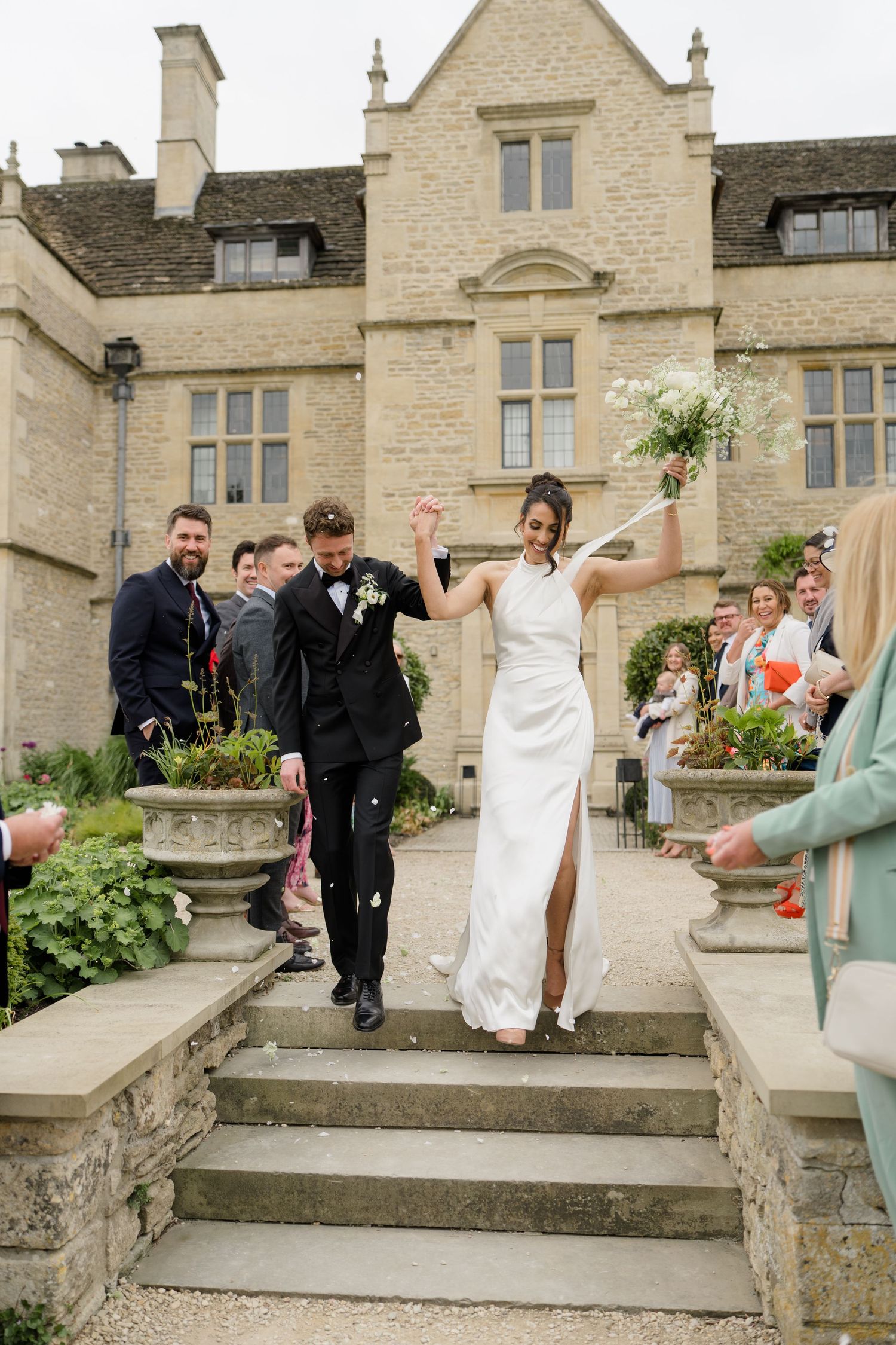 Newlyweds descend stone steps of elegant manor house as guests shower them with confetti.