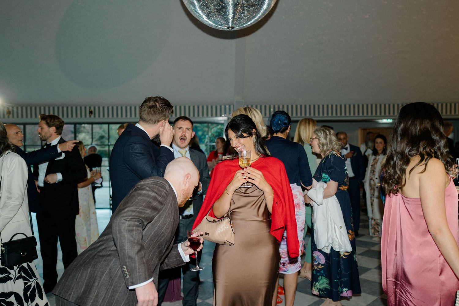 Wedding reception guests mingle and socialize in elegant white venue under disco ball lighting.