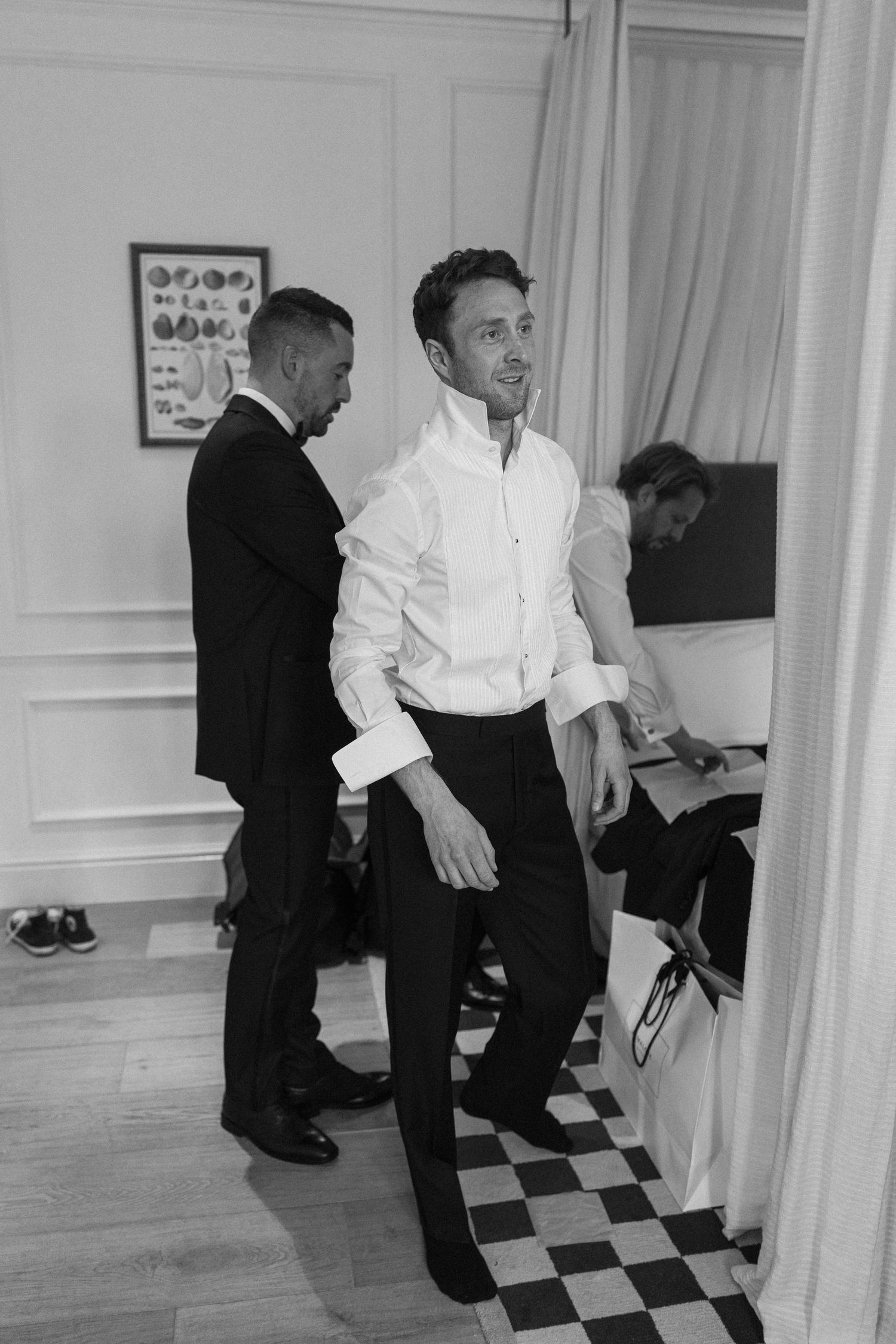 Black and white photo of groomsmen getting ready in a classic room with checkered floor.