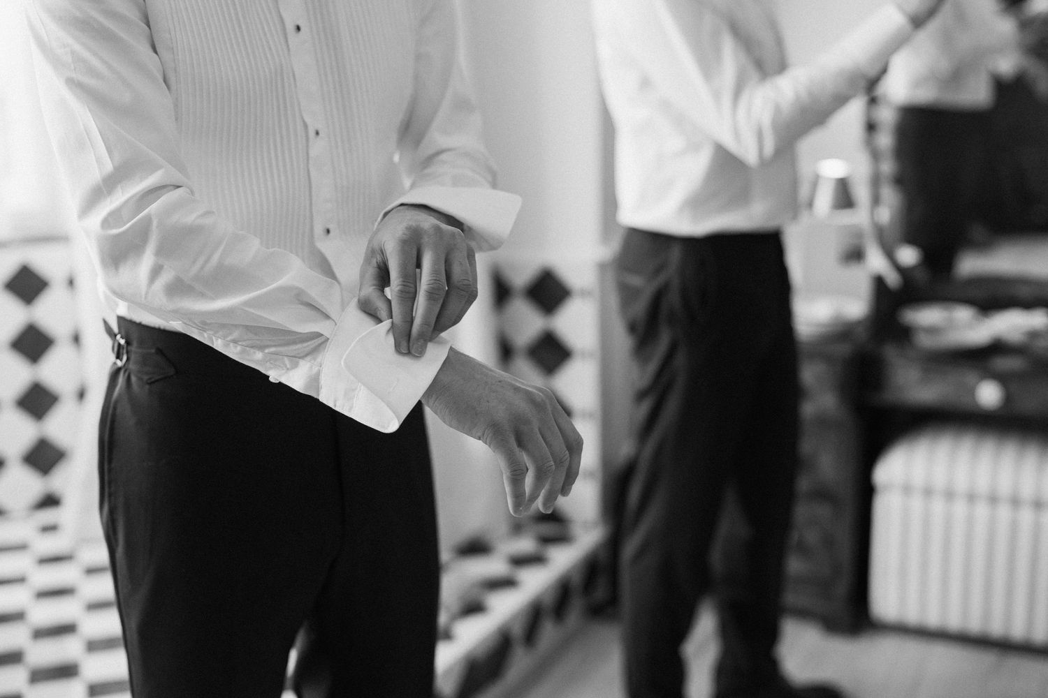 Close-up of groom fastening his cufflinks while another groomsman prepares in the background.