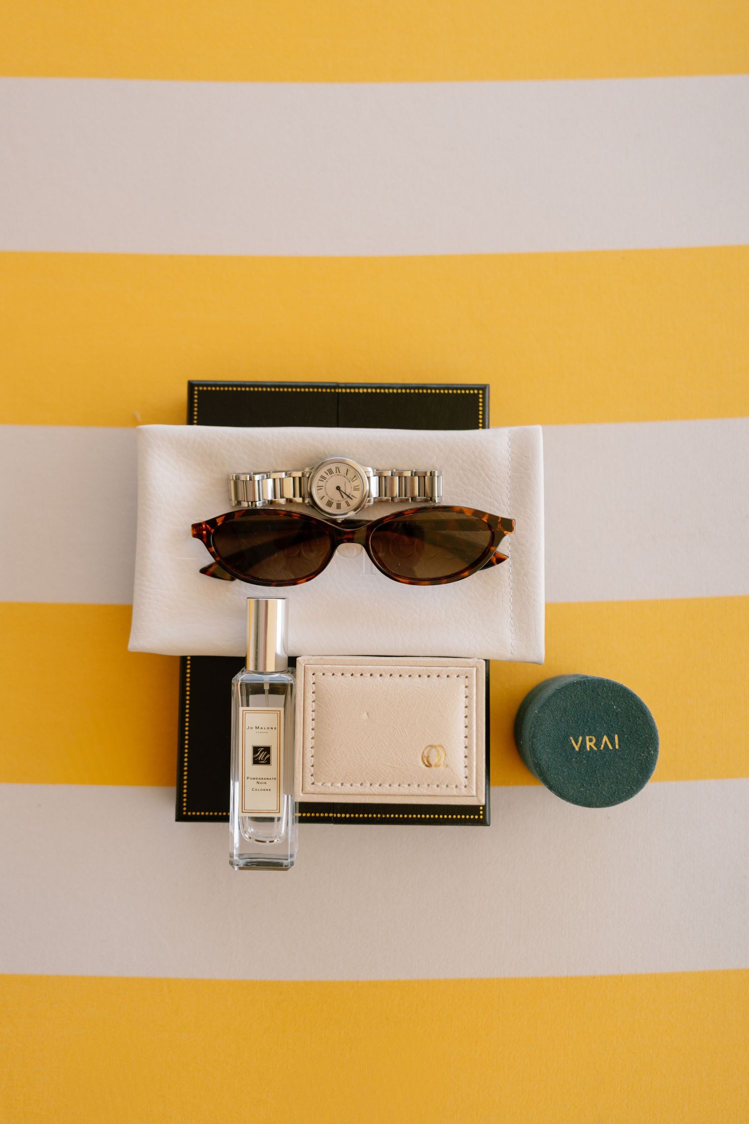 Perfume bottles, sunglasses and accessories arranged on yellow and white striped background.