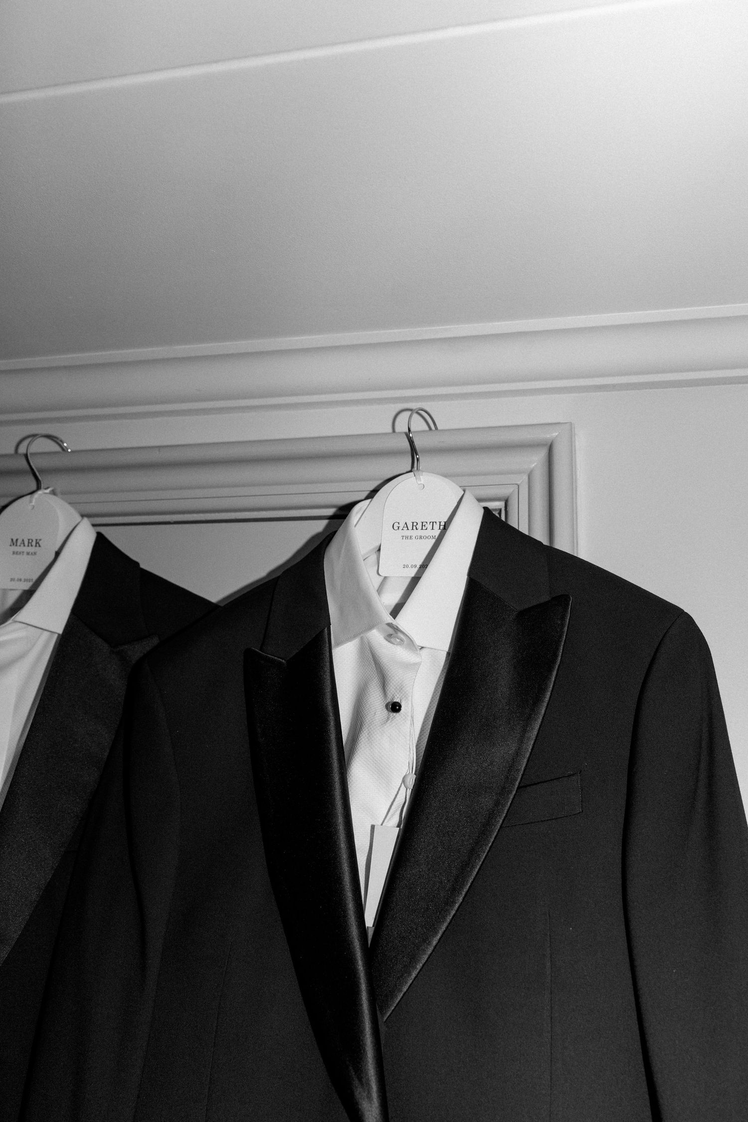 Classic black tuxedo jacket with white dress shirt hanging on display.