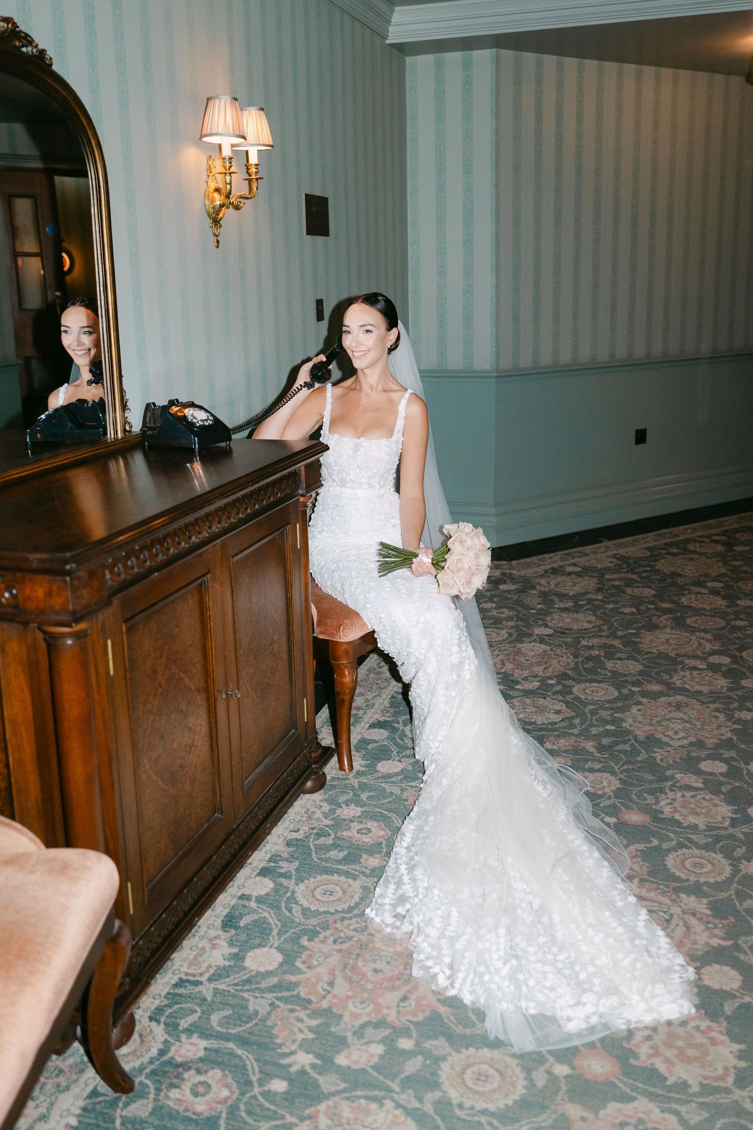 Bride in lace wedding dress poses dramatically against wooden paneling in hotel corridor.
