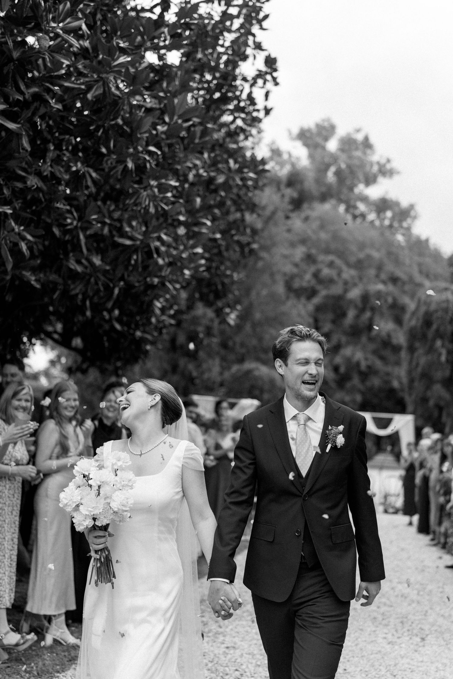 A black and white candid moment shows a couple sharing laughter during their wedding recessional.
