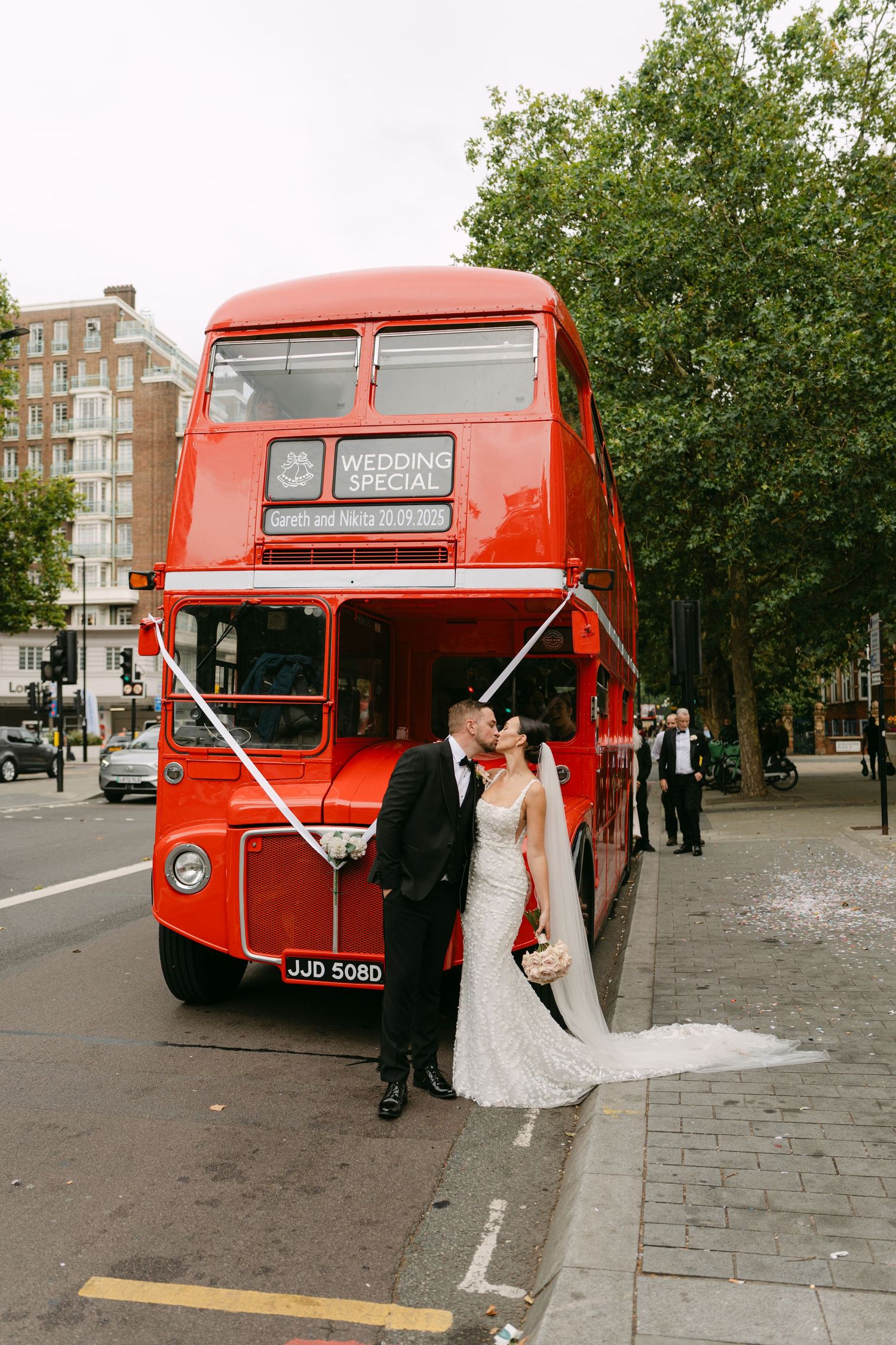 Classic red London double-decker bus decorated with wedding ribbons on a city street.