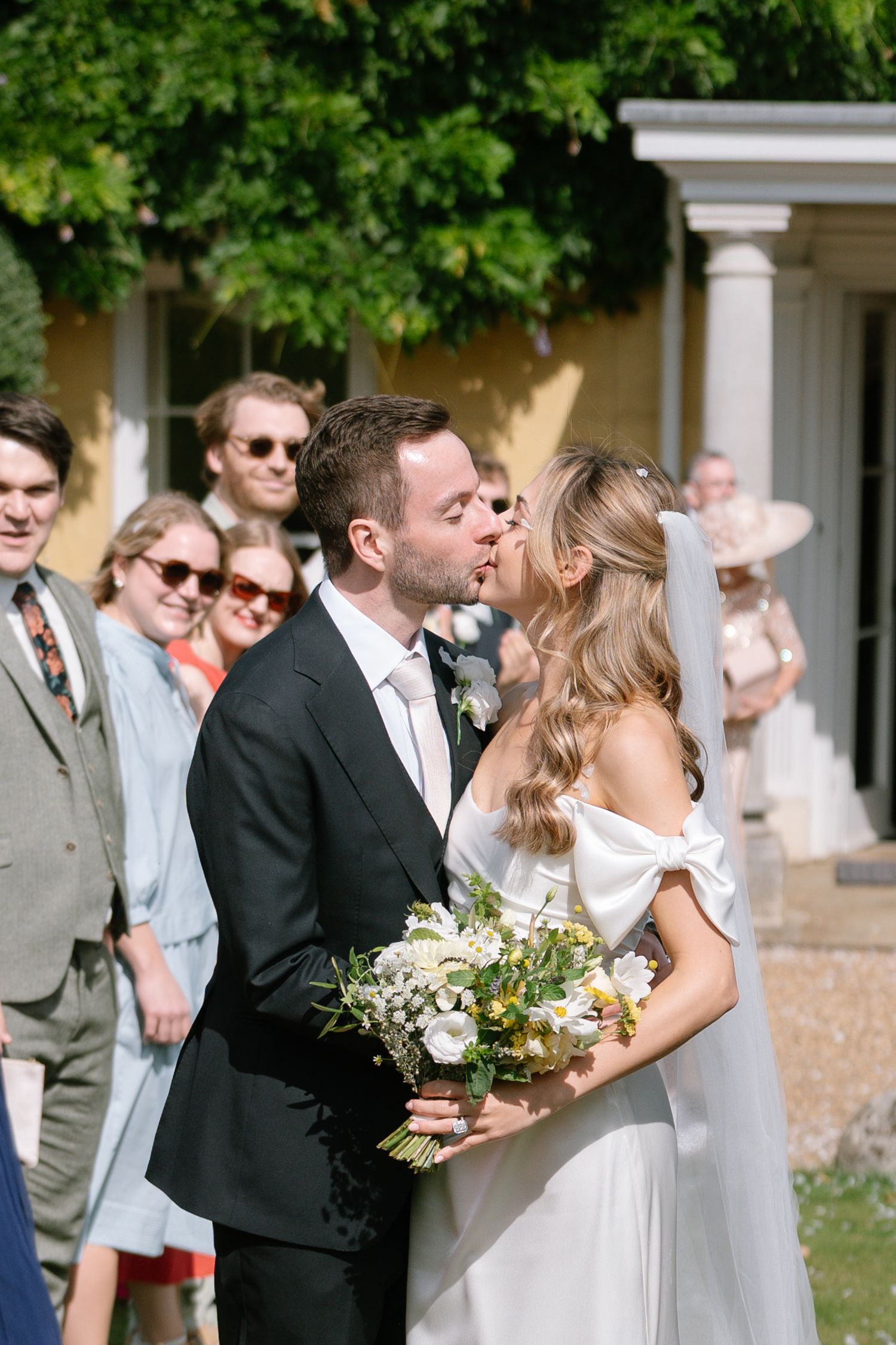 Wedding couple shares intimate moment while guests look on during outdoor celebration.