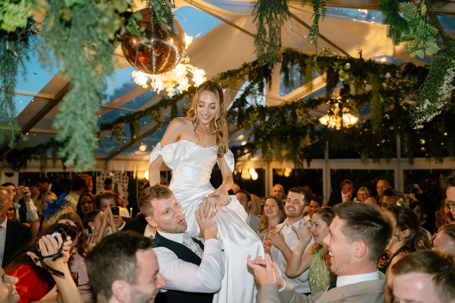 Wedding reception dance floor under greenery and string light decorations.