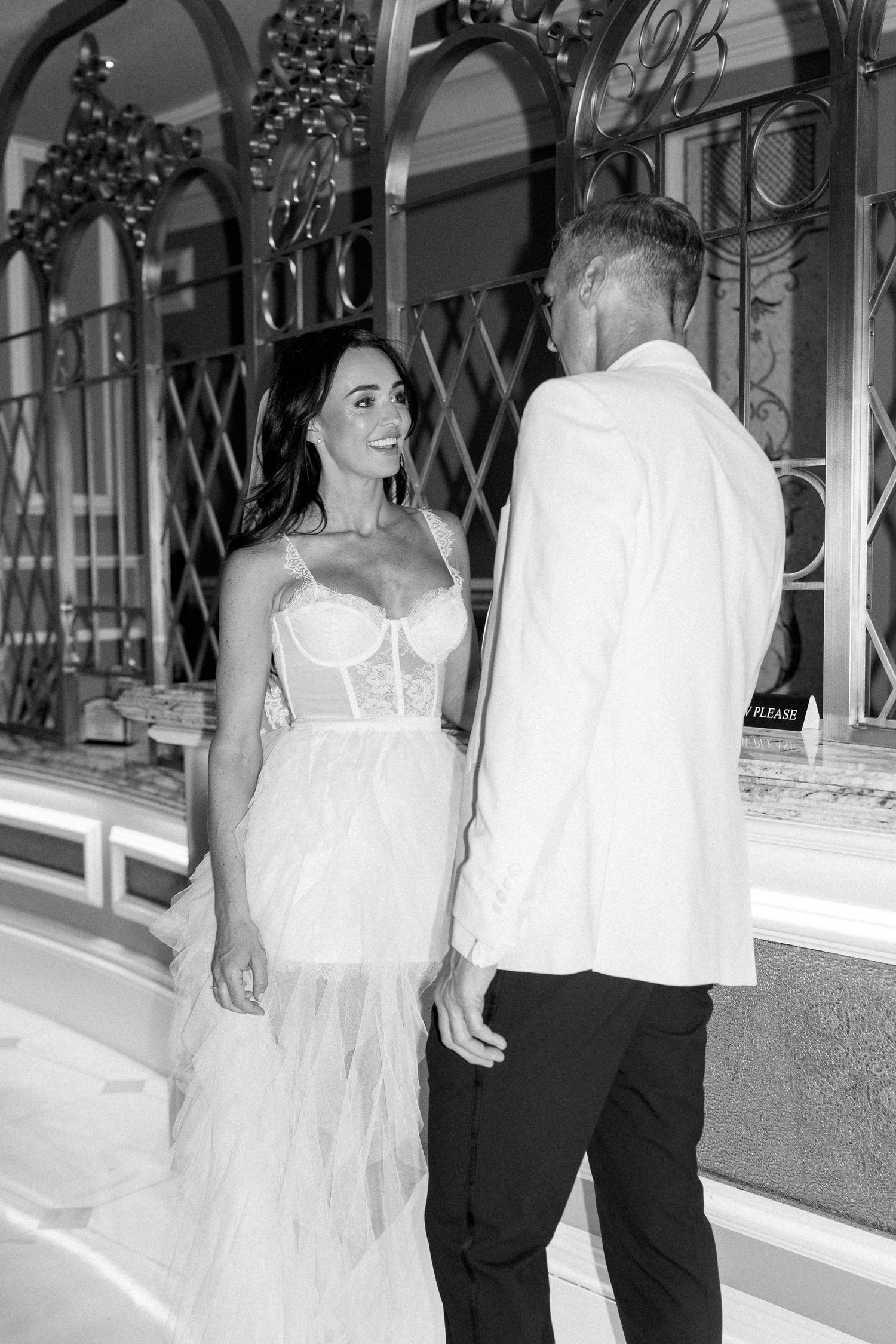 Black and white photo of a couple in wedding attire walking through a luxury retail corridor.