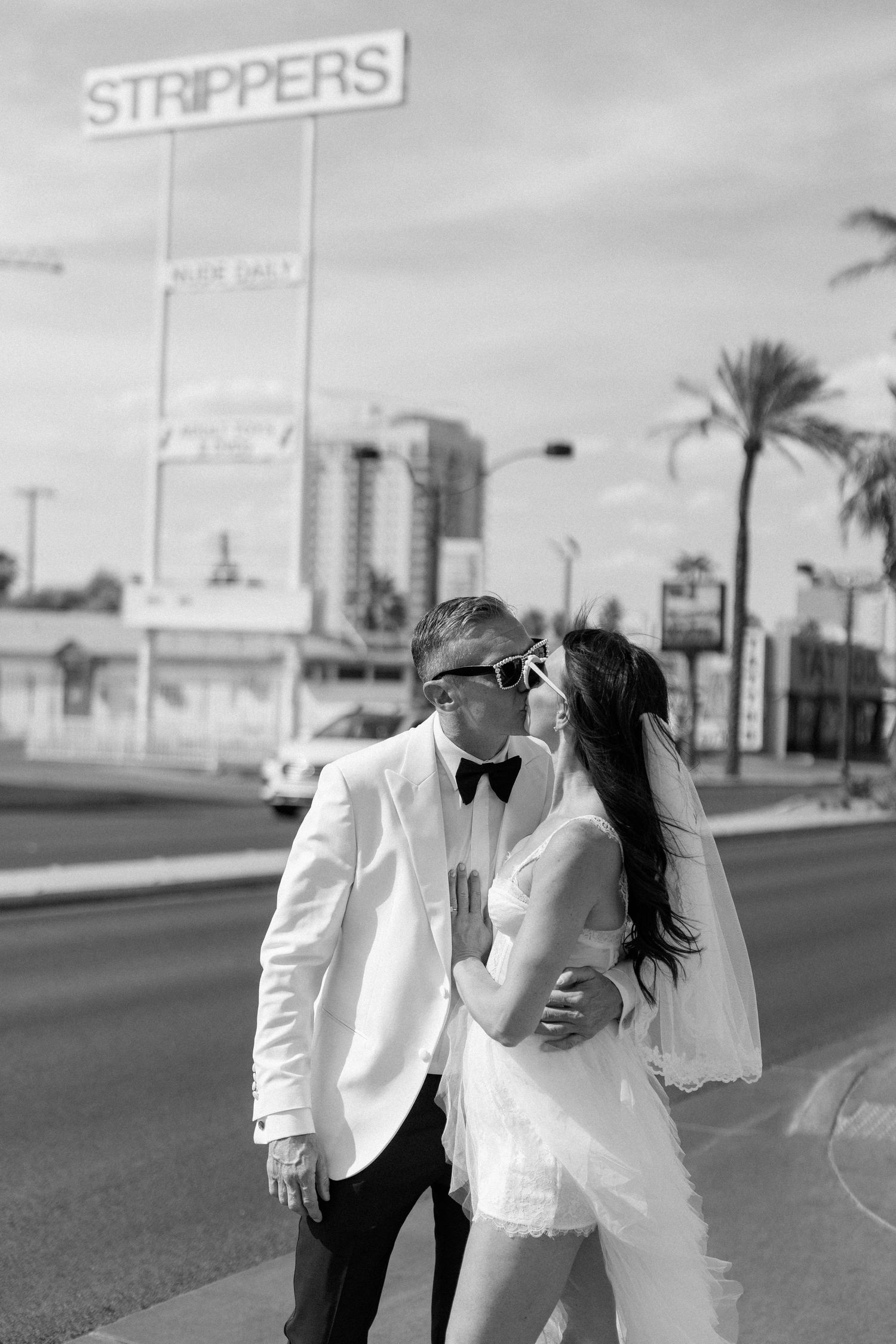 A wedding couple poses on a Las Vegas street with a vintage strip club sign in the background.