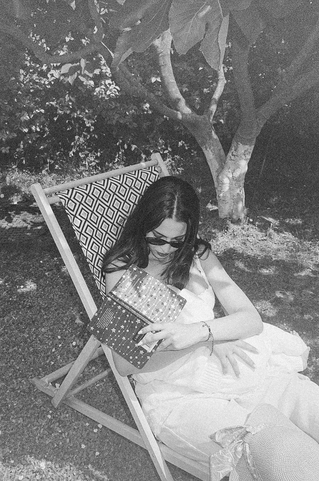 Woman in white dress relaxing on striped deck chair reading a book outdoors.