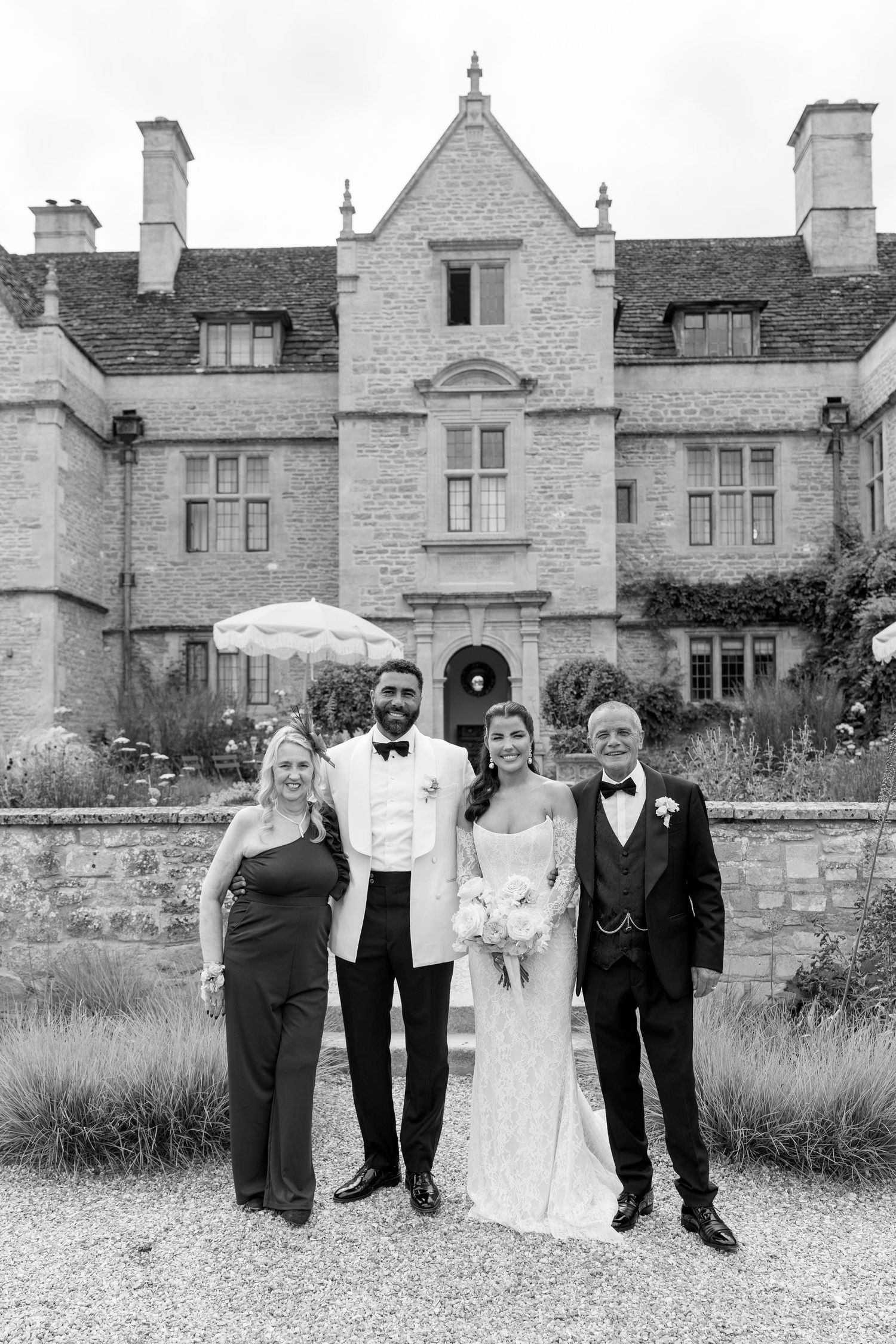 Wedding group photo with bride, groom, and family posing before grand stone manor house.