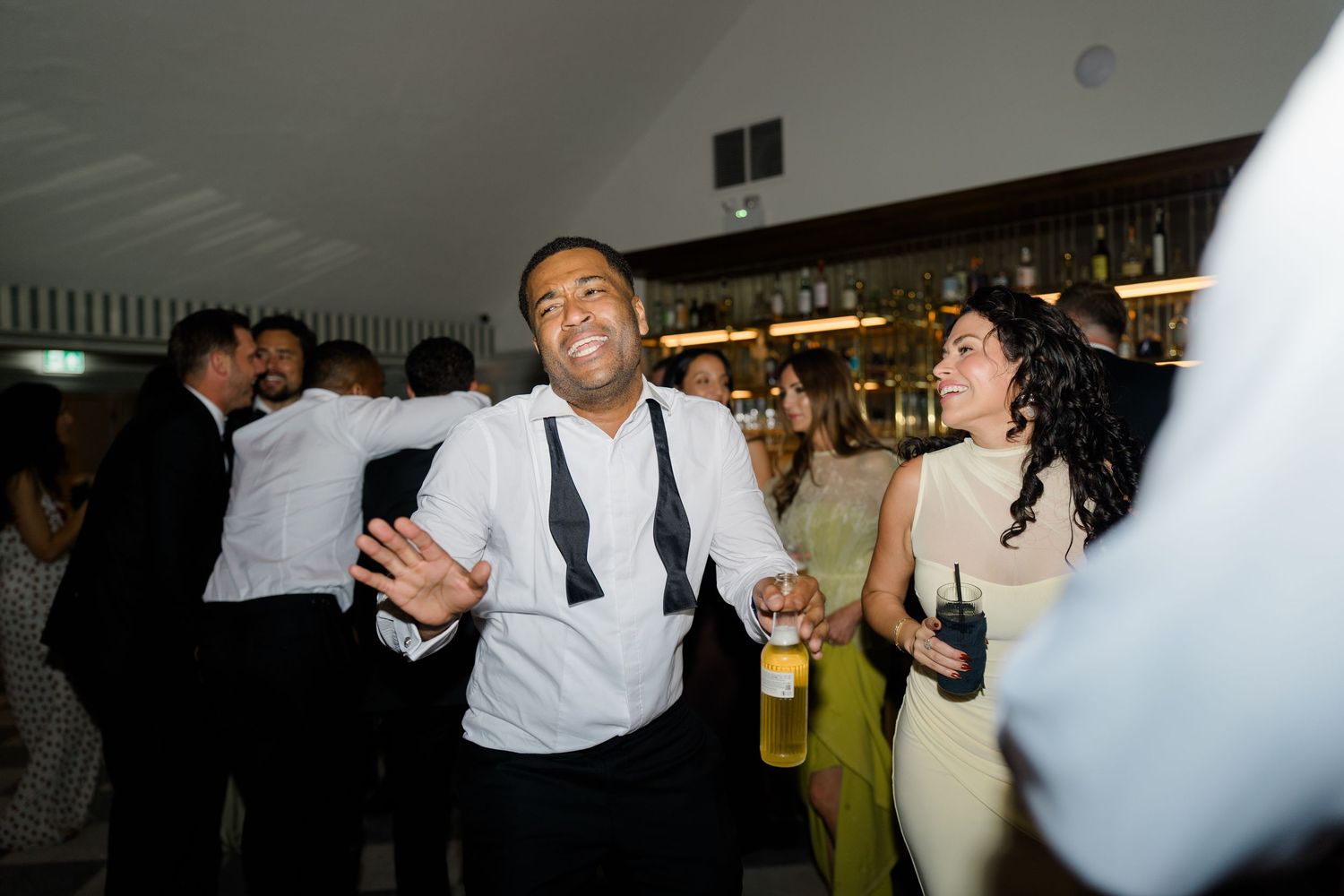 Wedding guest dancing energetically with a drink in hand at a lively indoor reception party.