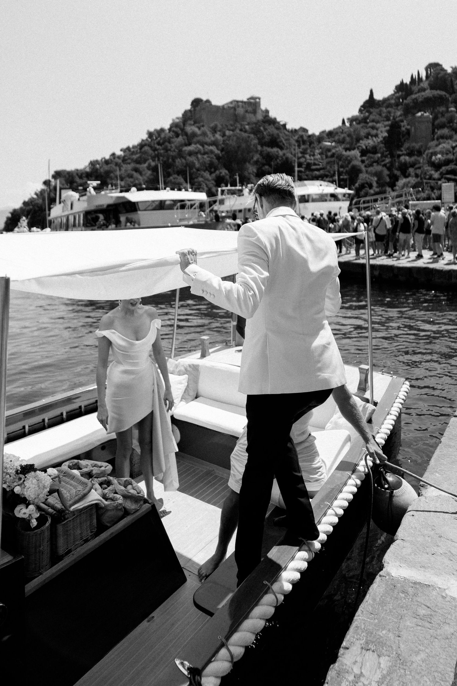 Black and white photo of bride and groom boarding a luxury white boat at an Italian coastal wedding.