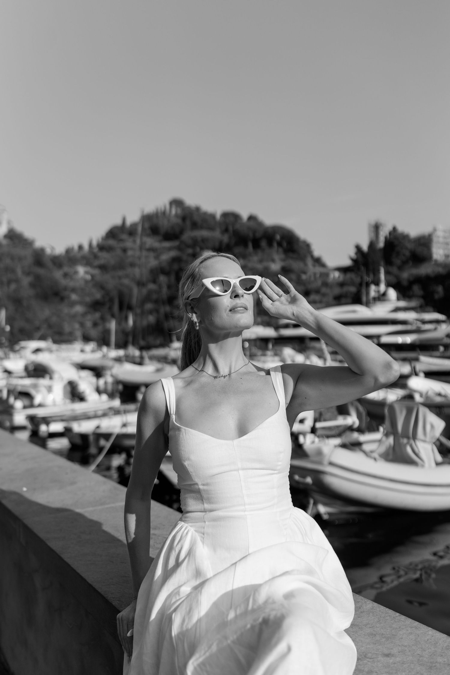 Black and white portrait of woman in white dress adjusting sunglasses by Portofino marina.