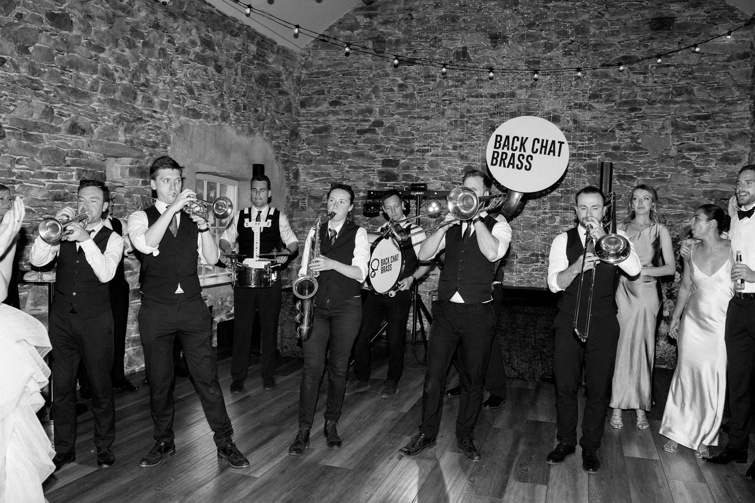 Wedding party groomsmen perform a choreographed dance routine in a rustic stone-walled venue.