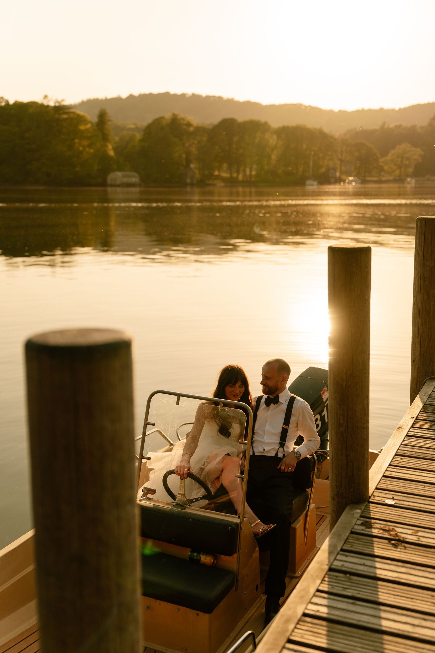 Couple in wedding attire sitting on dock during golden hour with lake views.