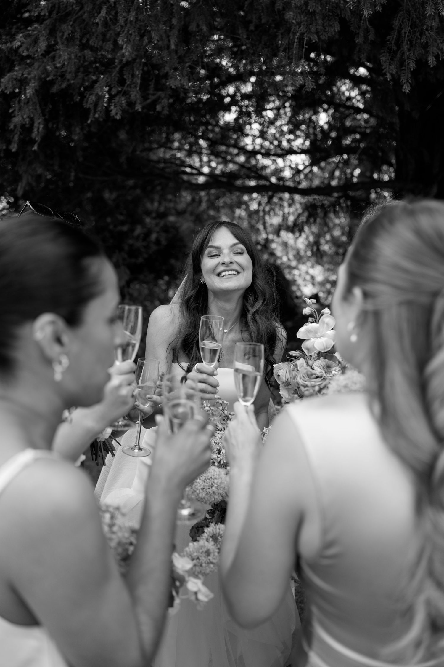 Wedding party members share laughter and drinks during an outdoor reception.