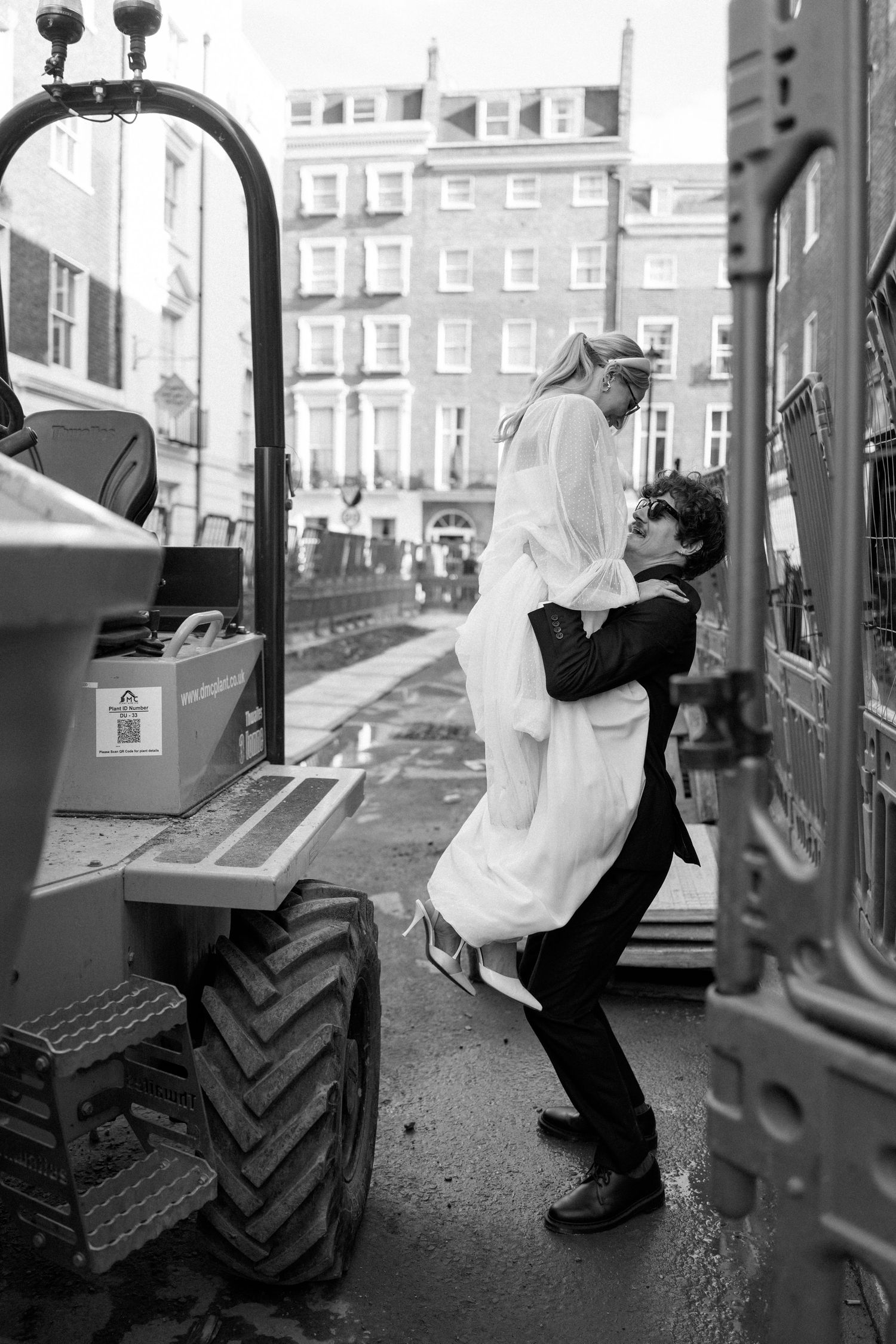 Black and white photo of newlyweds posing on construction equipment.