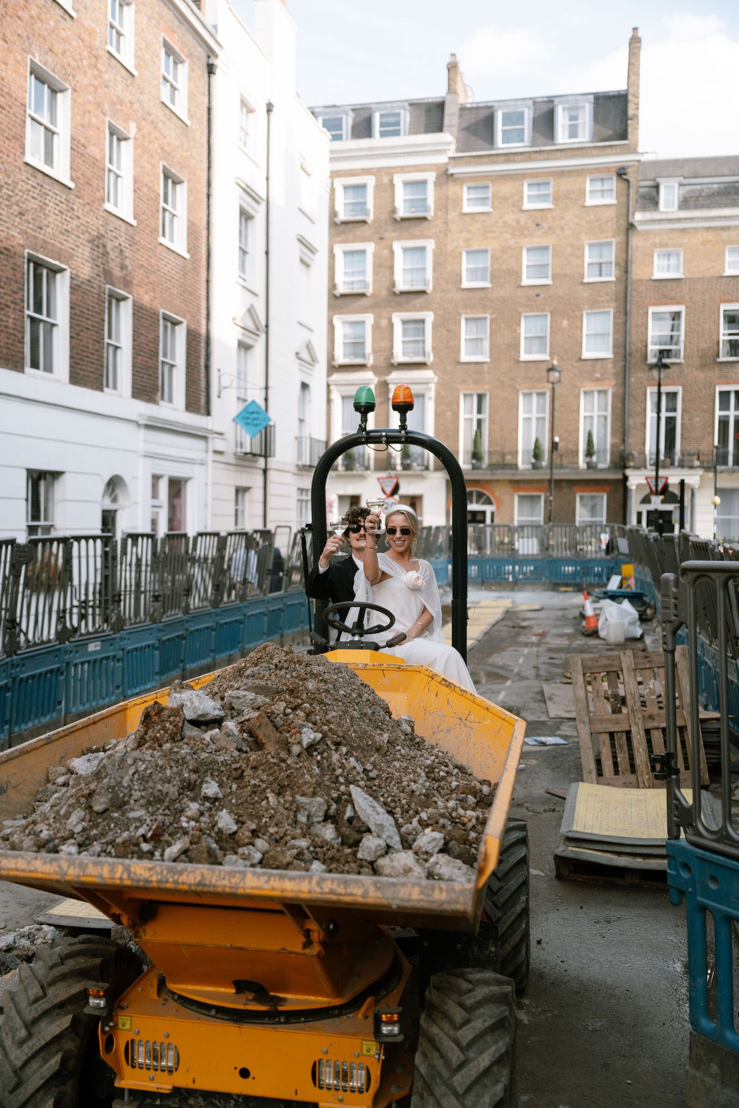 A yellow construction vehicle loaded with debris parked between brick buildings.