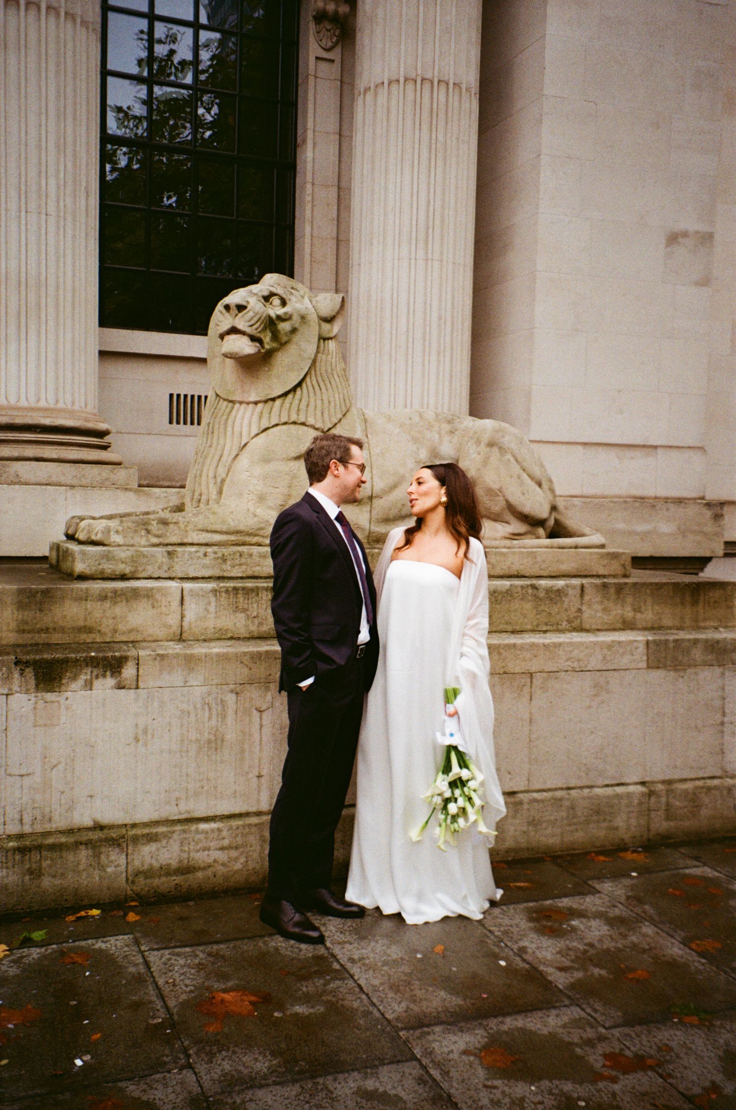 Romantic wedding couple embracing against a classical stone building with columns.