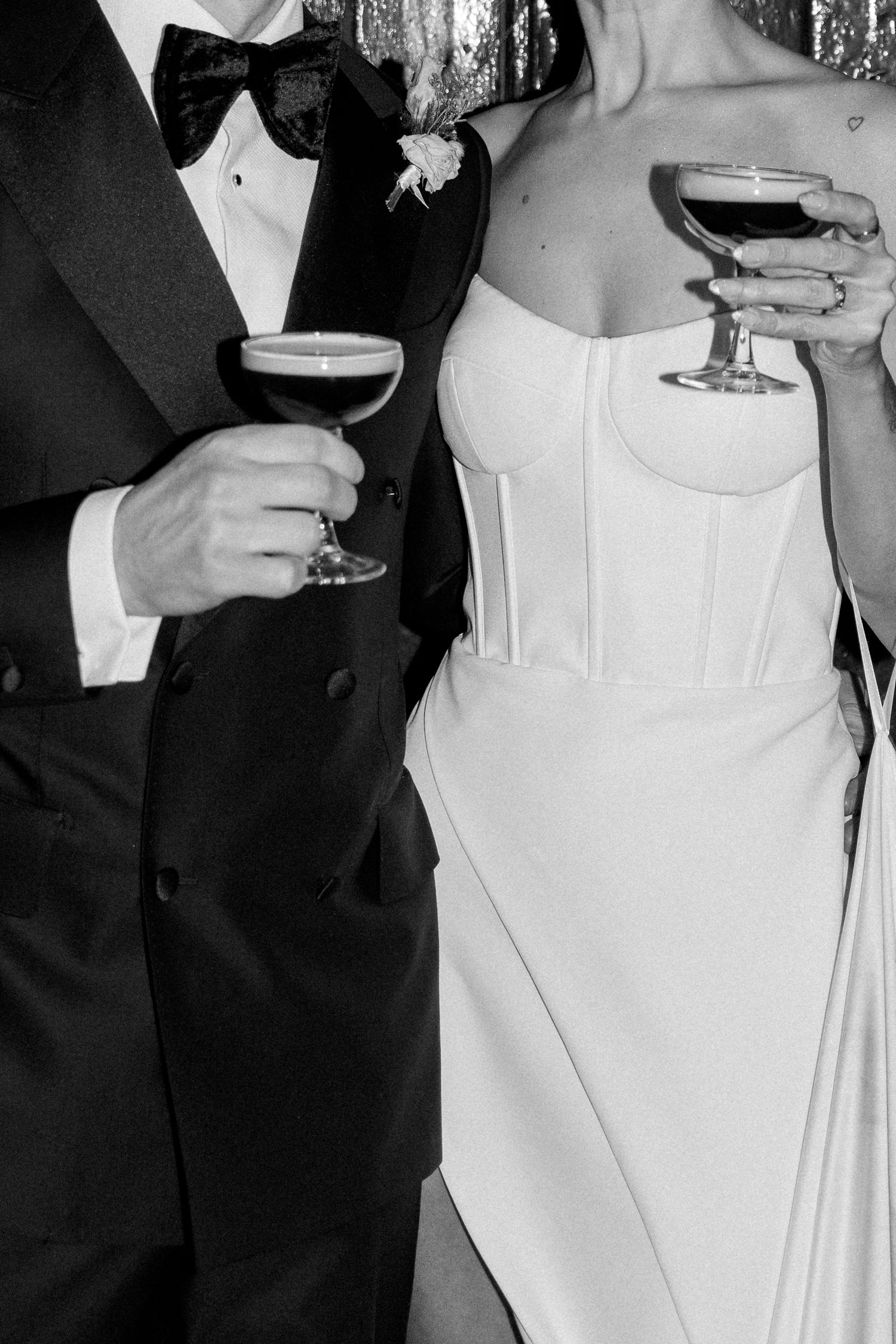 People in formal attire hold champagne glasses at an elegant party with a sparkly silver backdrop.