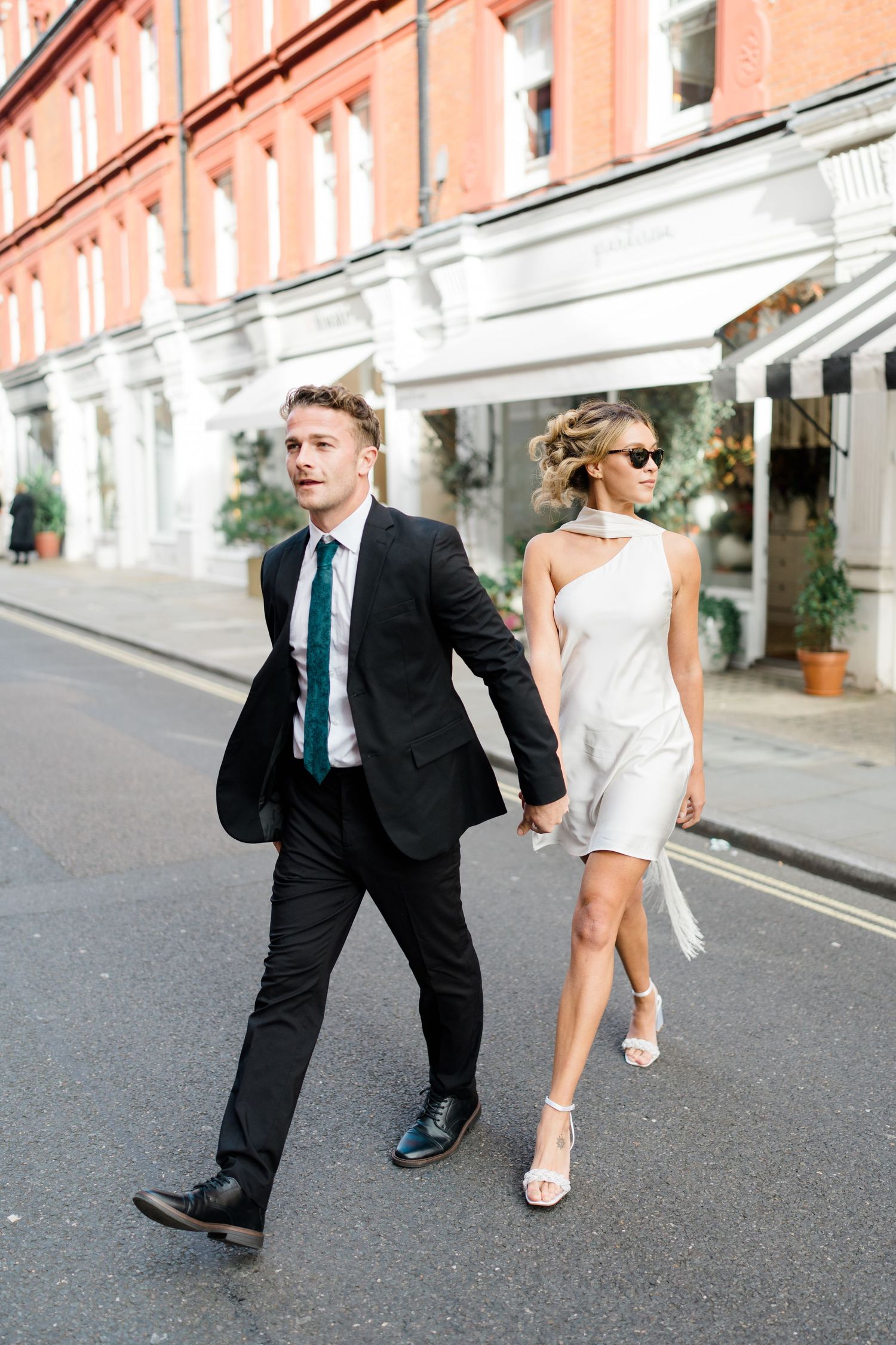 A couple in formal attire playfully poses on a city street.