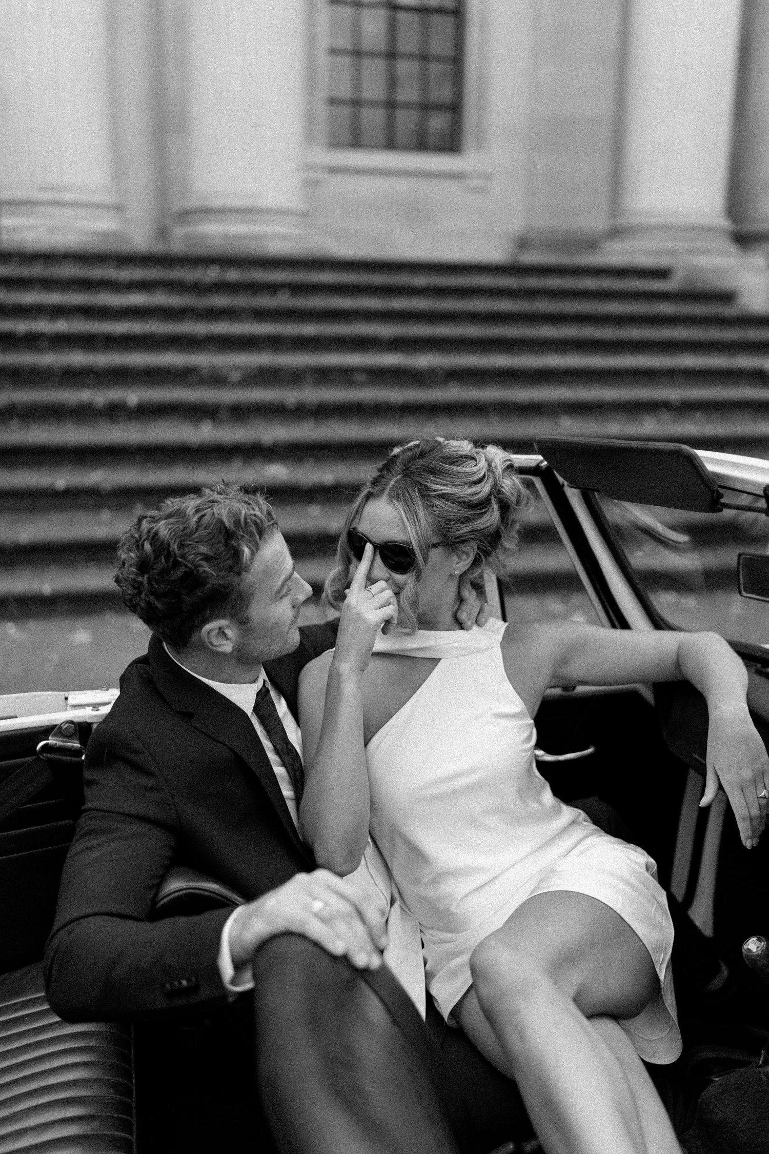 A couple shares an intimate moment near a classic car.