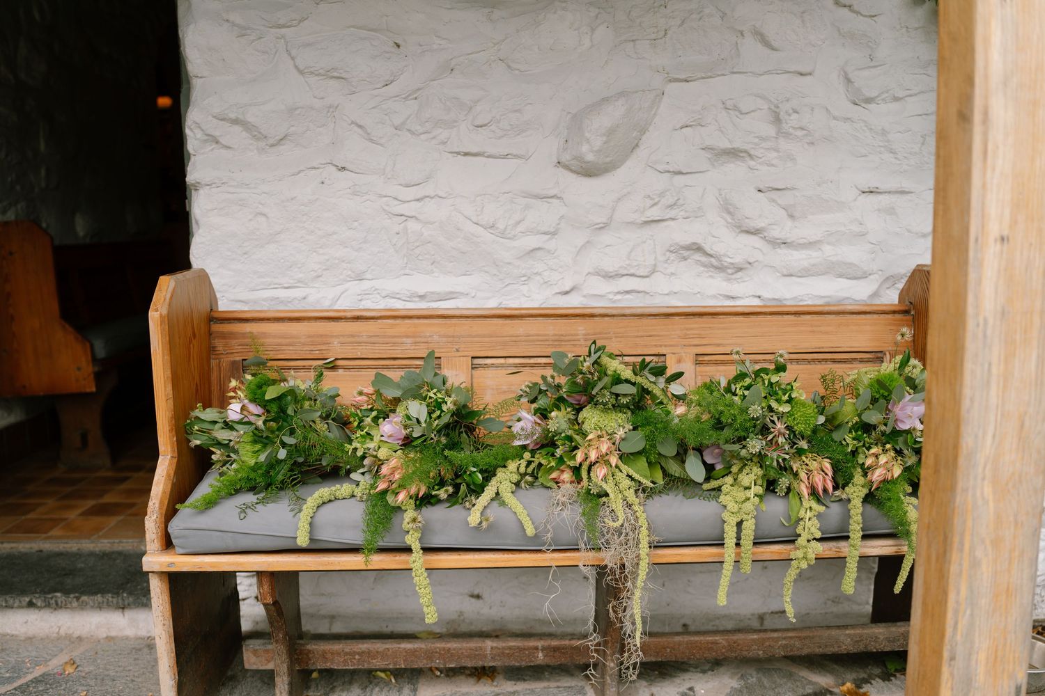 Rustic wooden bench decorated with fresh greenery and floral arrangements.