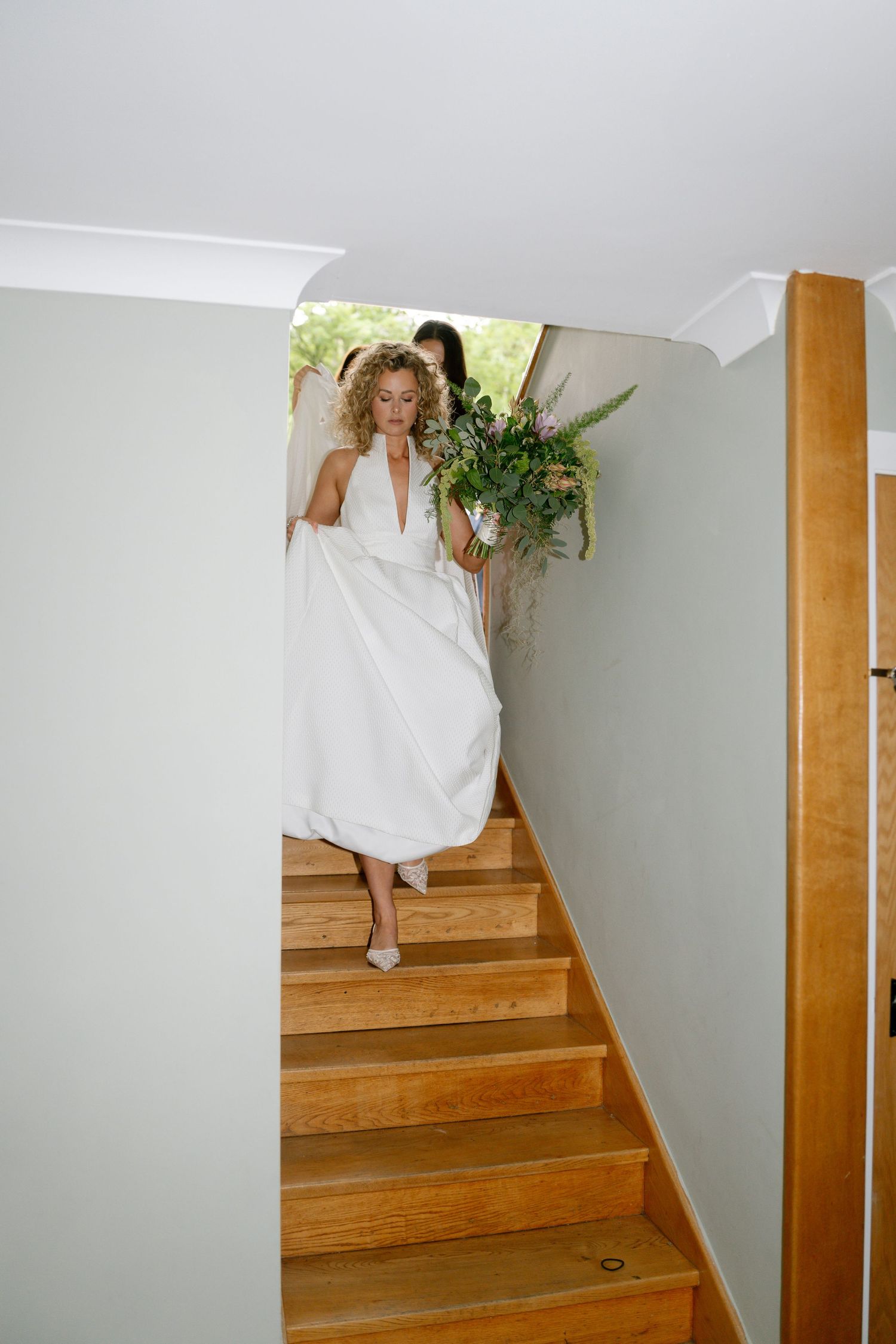 White wedding dress flowing down wooden stairs in a minimalist interior setting.