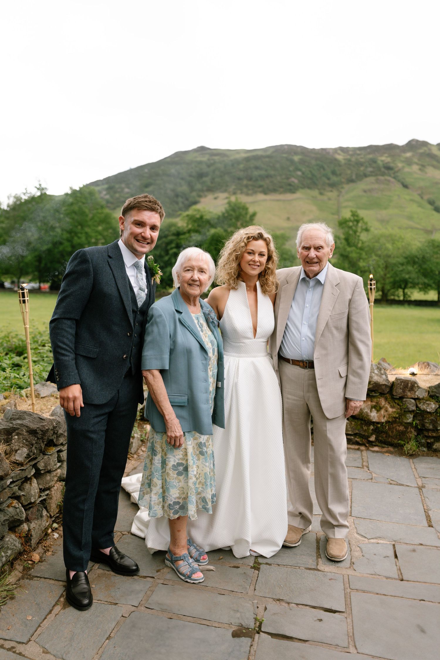 Wedding group portrait with family members against stone wall and mountain backdrop.