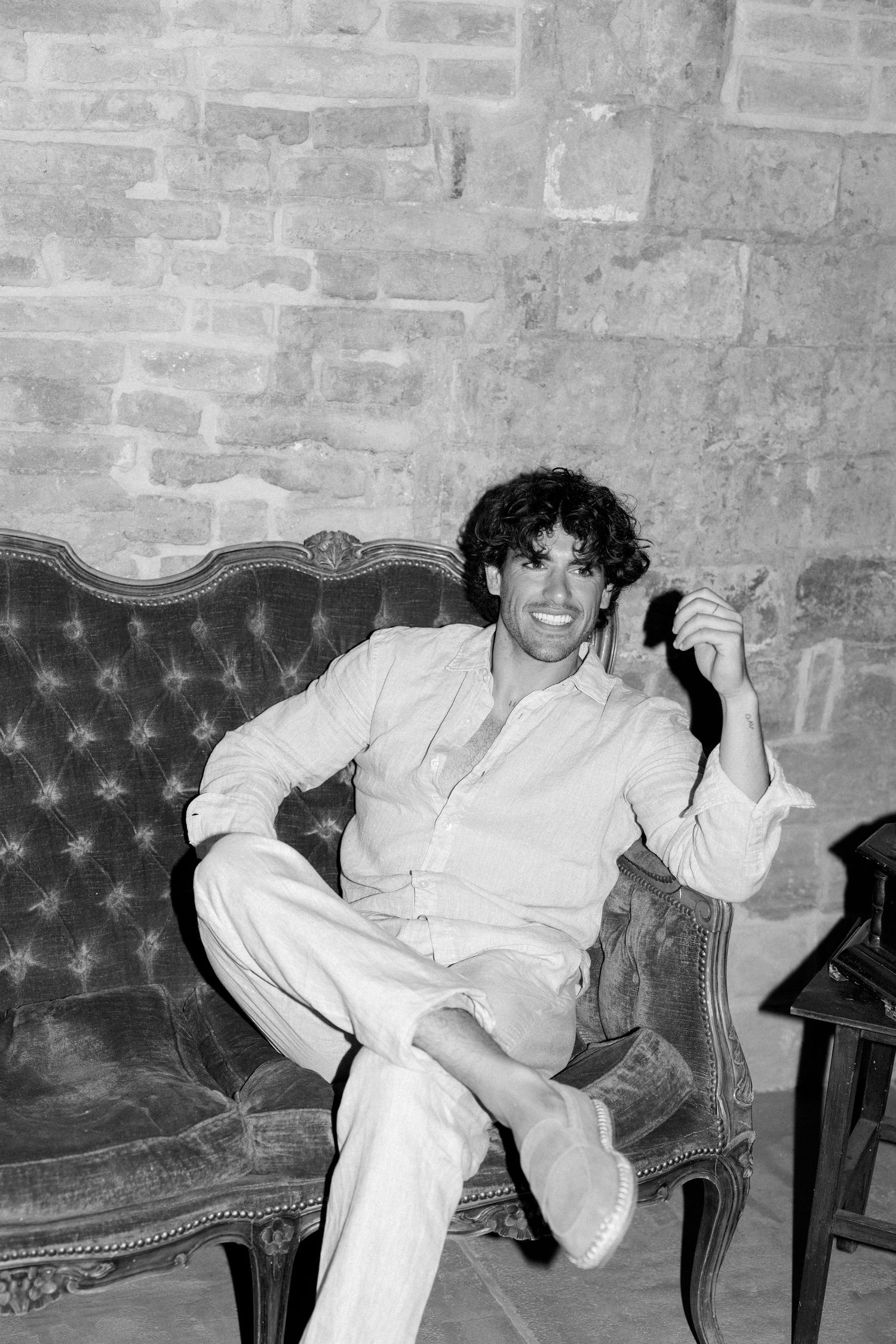A person lounges casually on a vintage leather sofa against an exposed brick wall.