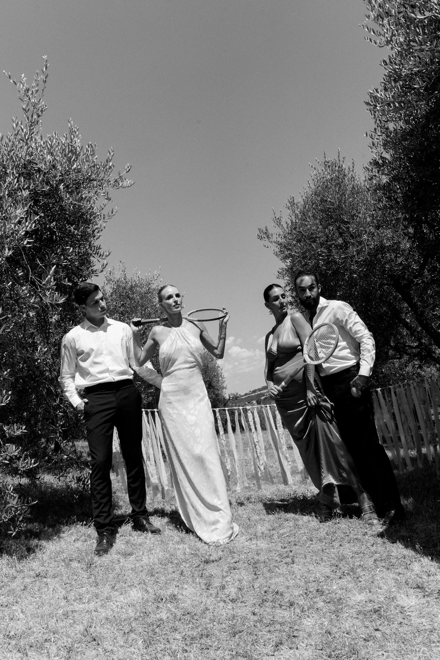 Wedding party enjoying candid moments in a scenic olive grove on a sunny day.